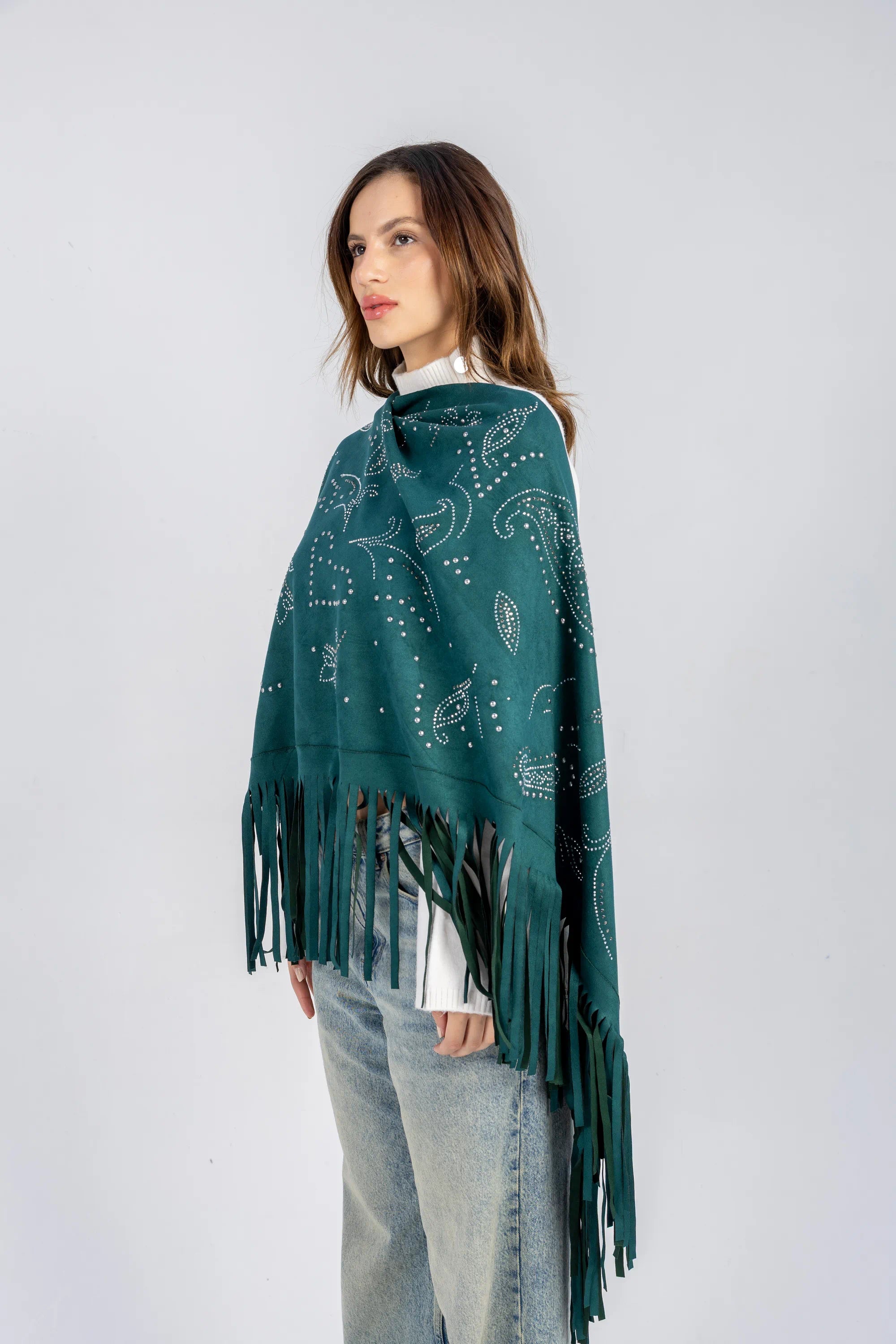 Woman wearing a teal poncho with fringe details on a white background
