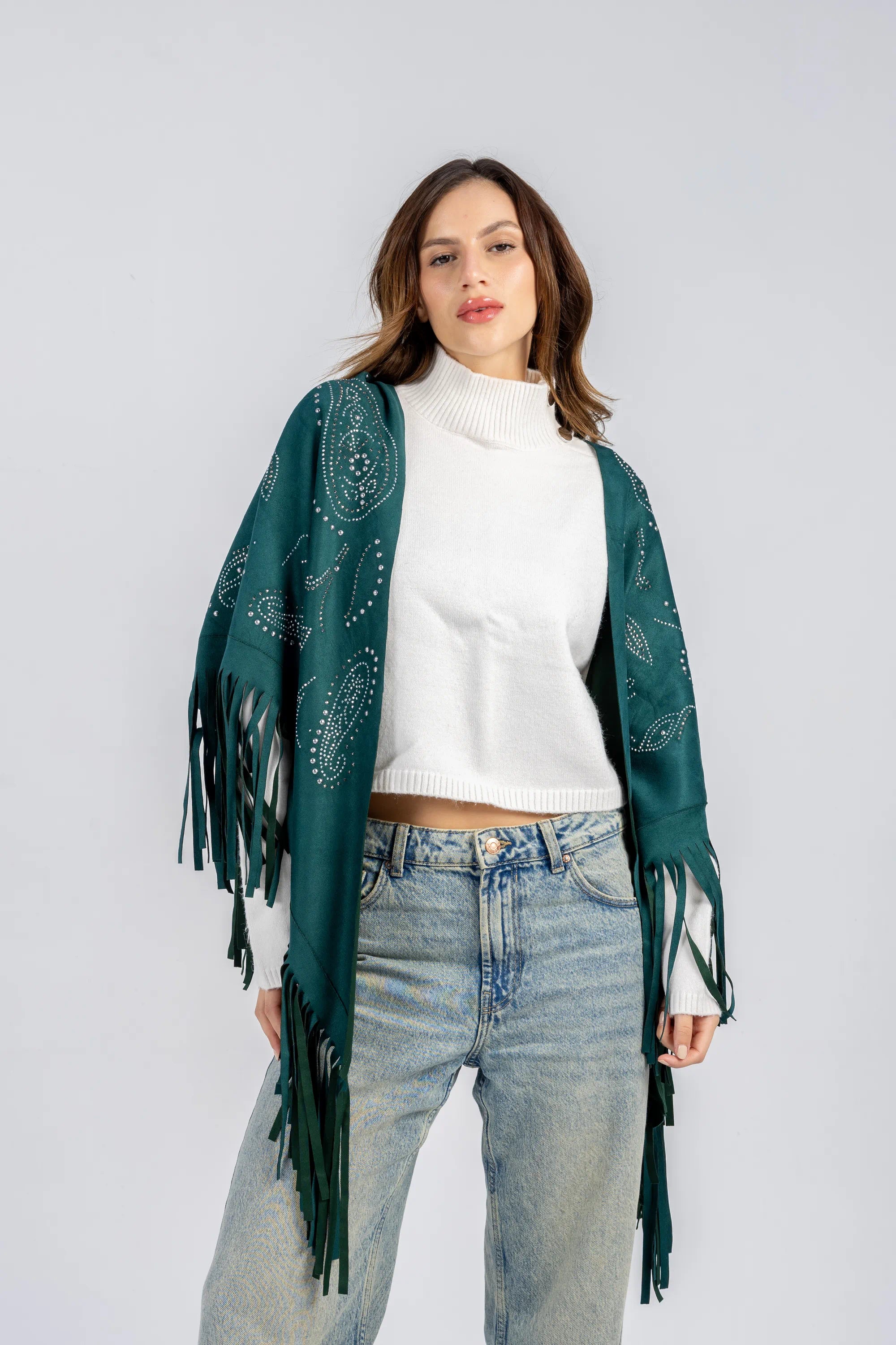 Woman wearing a green patterned shawl over a white top and blue jeans on a light gray background