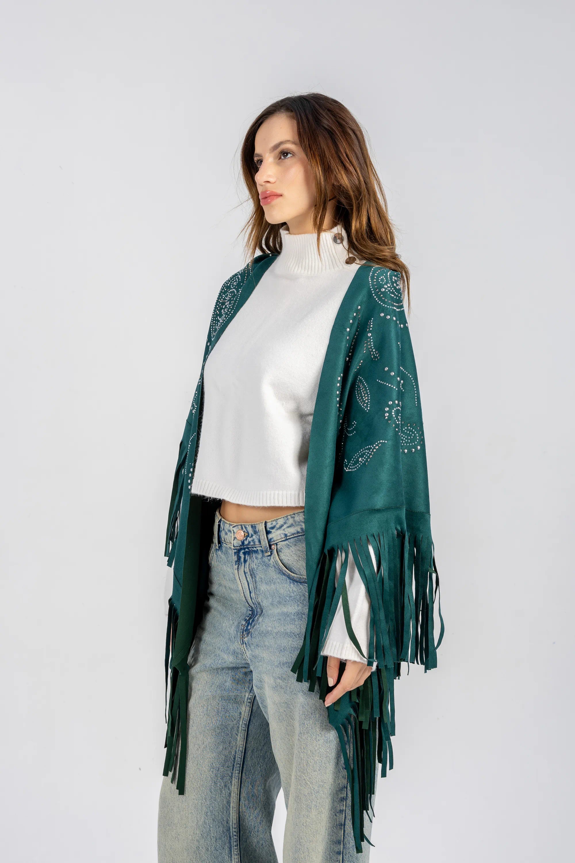 Woman wearing a green fringed shawl over a white top and blue jeans on a light gray background