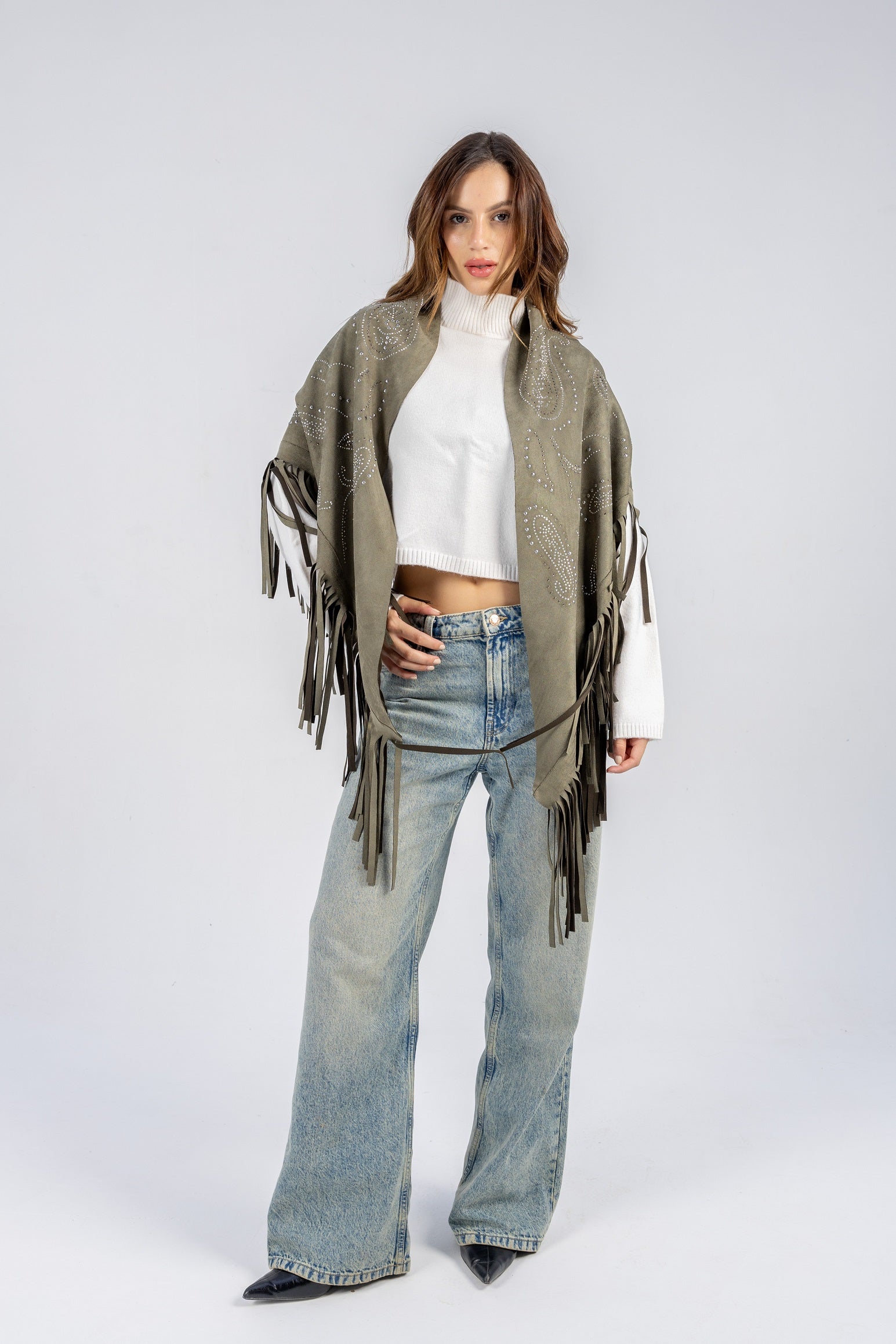 Woman wearing a green fringe poncho over a white top and blue jeans on a white background