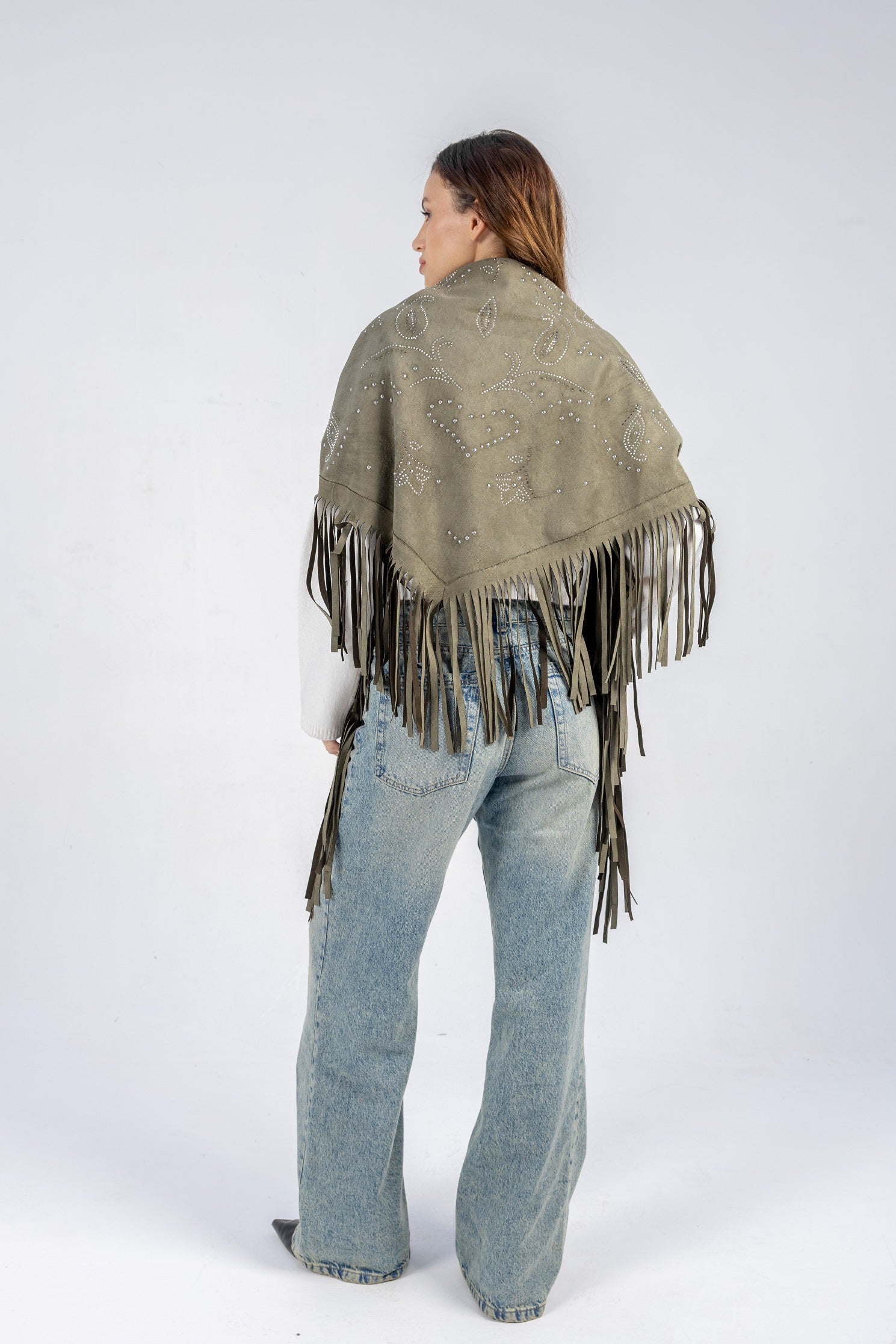 Person wearing a patterned shawl with fringes and jeans on a white background