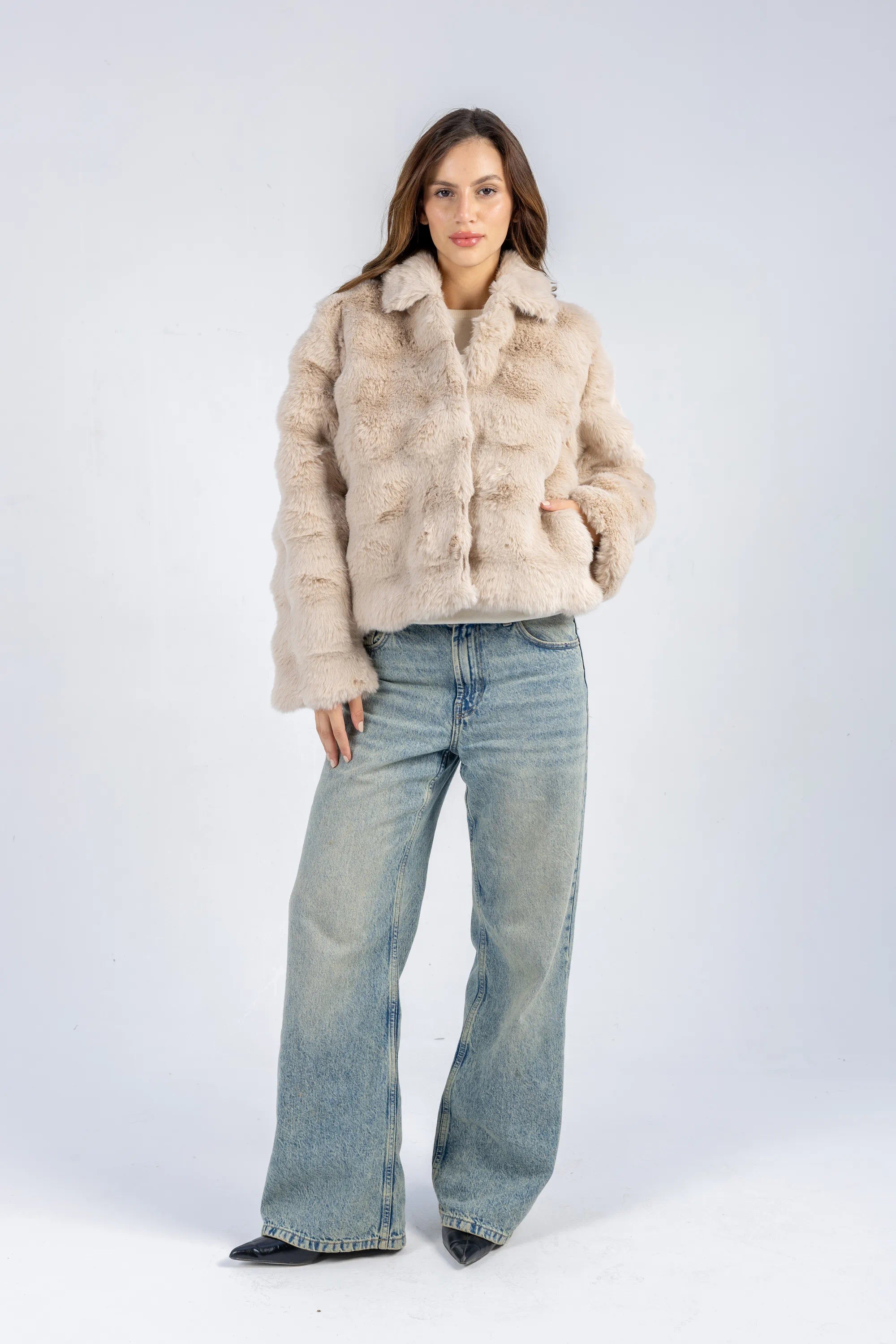 Woman wearing a beige fur jacket and blue jeans on a white background