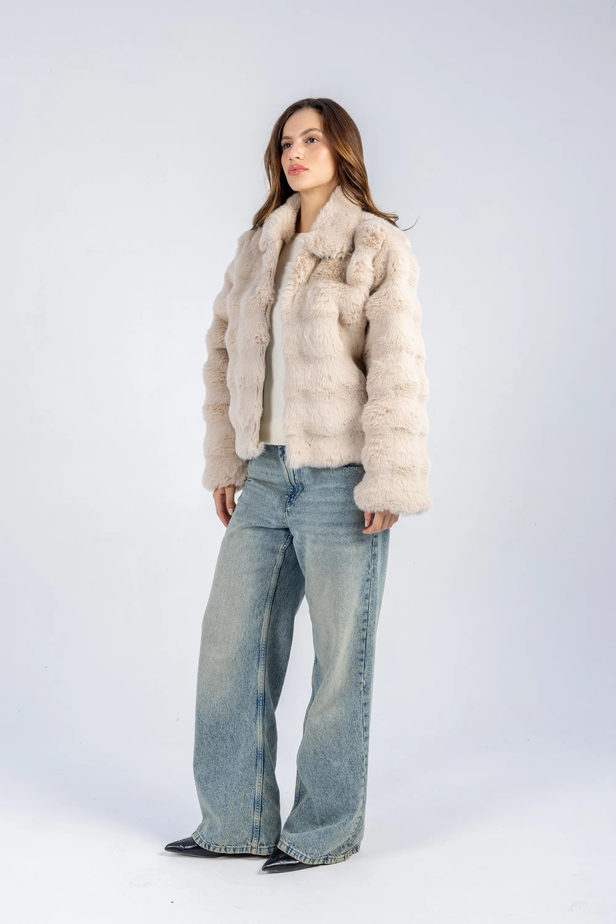 Woman wearing a beige fur coat and blue jeans on a white background