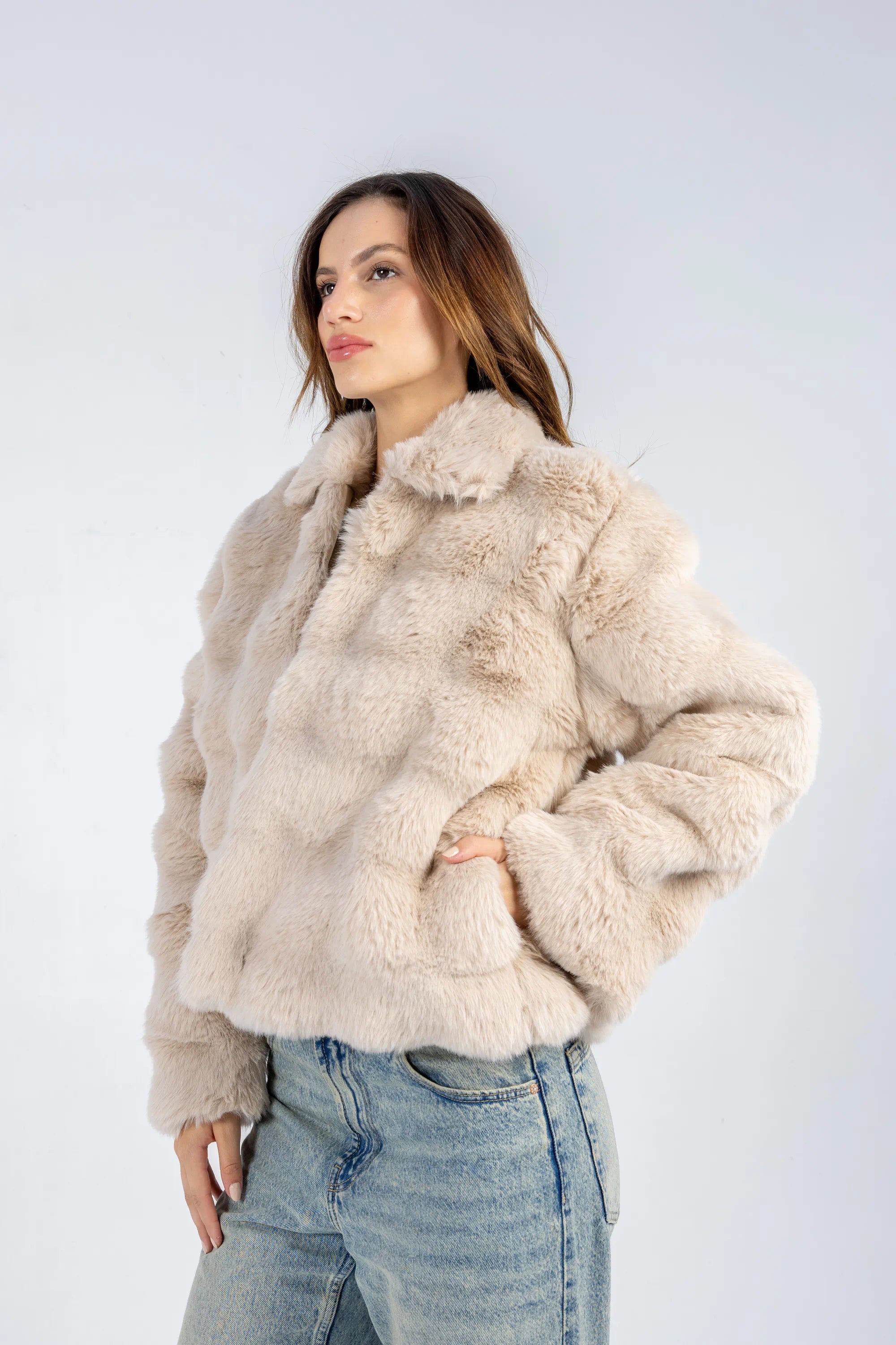 Woman wearing a beige fur jacket and jeans on a white background