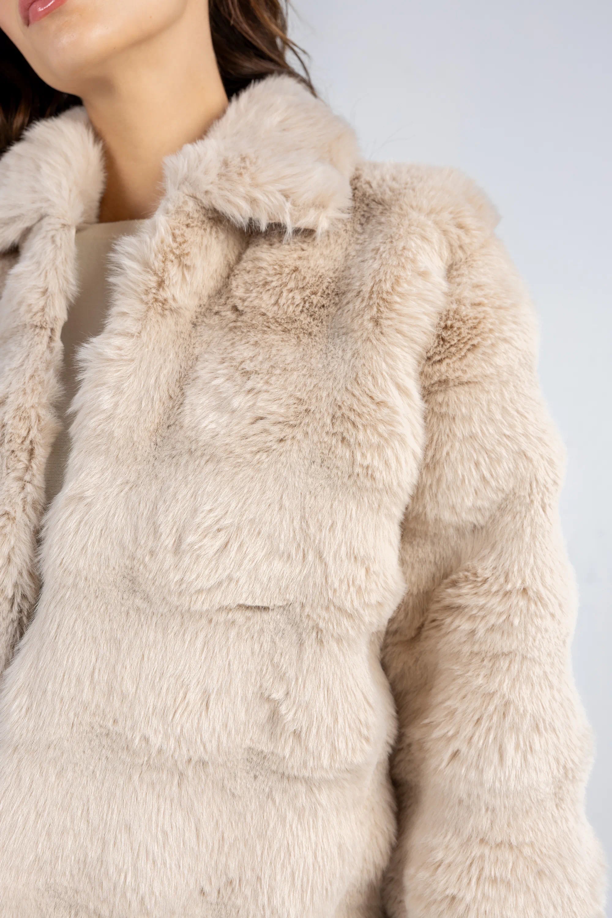 Close-up of a beige fur vest worn by a person on a light gray background