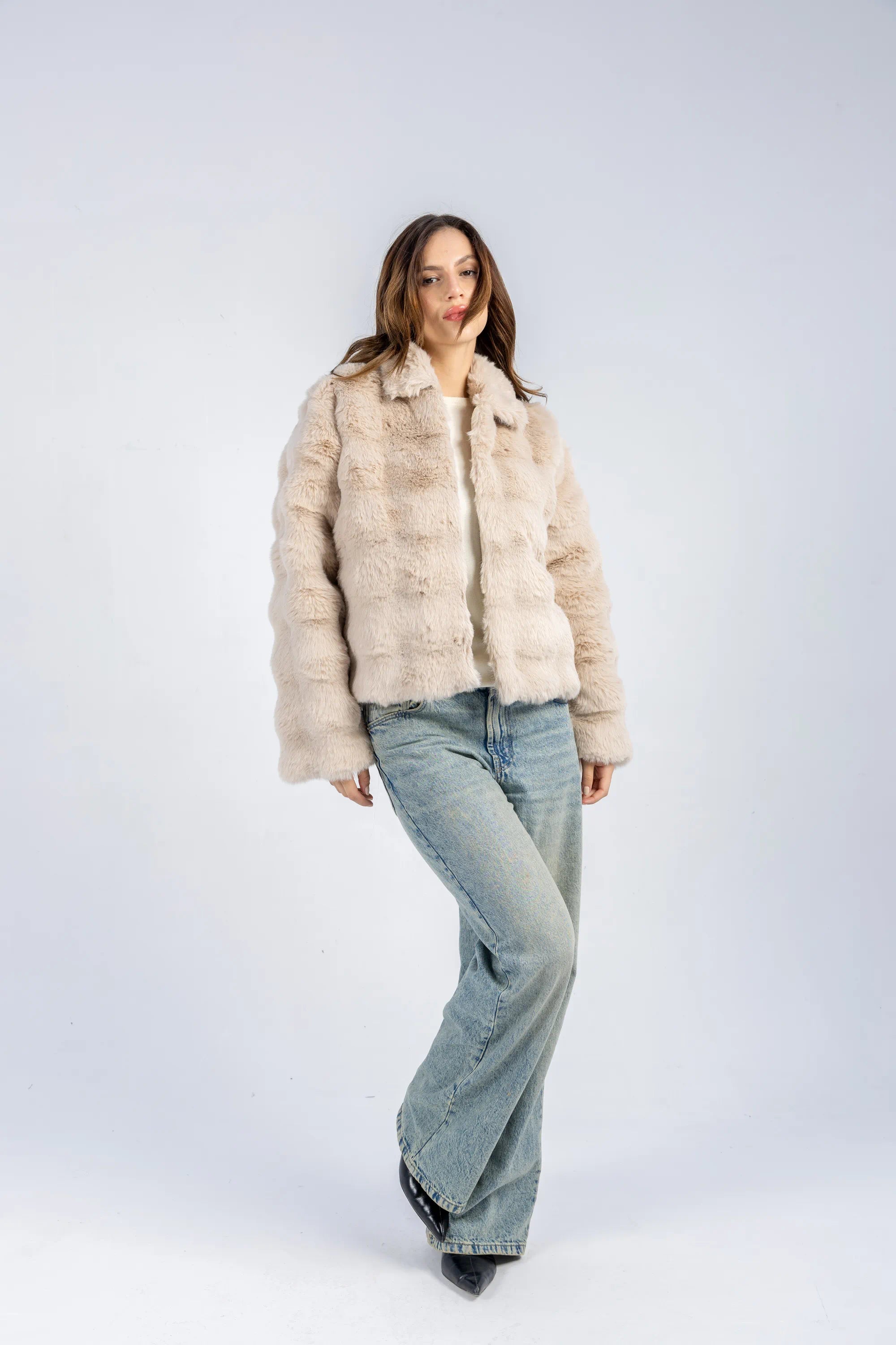 Woman wearing a beige fur coat and light blue jeans on a white background