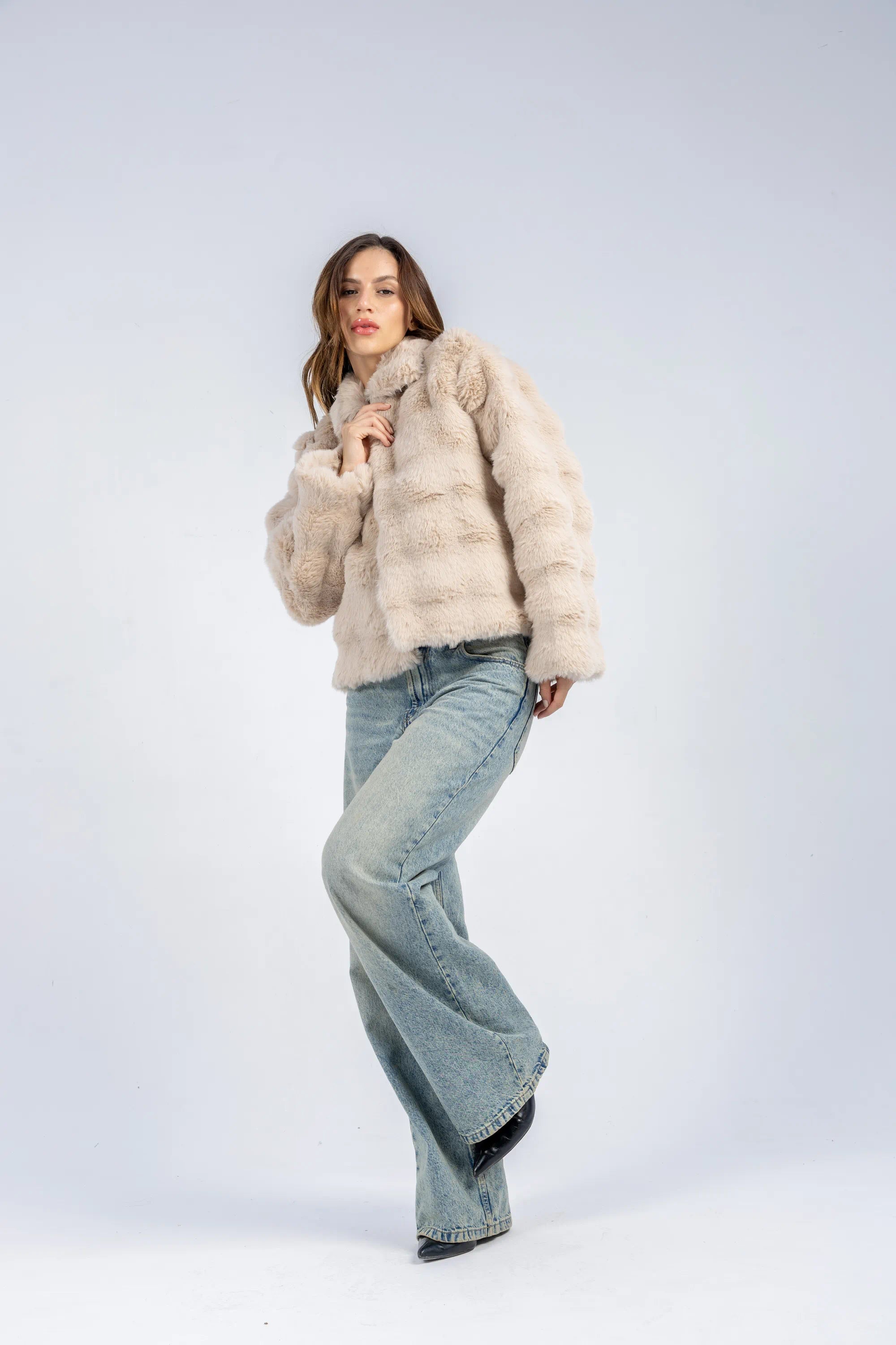 Woman wearing a light-colored fur coat and jeans on a white background