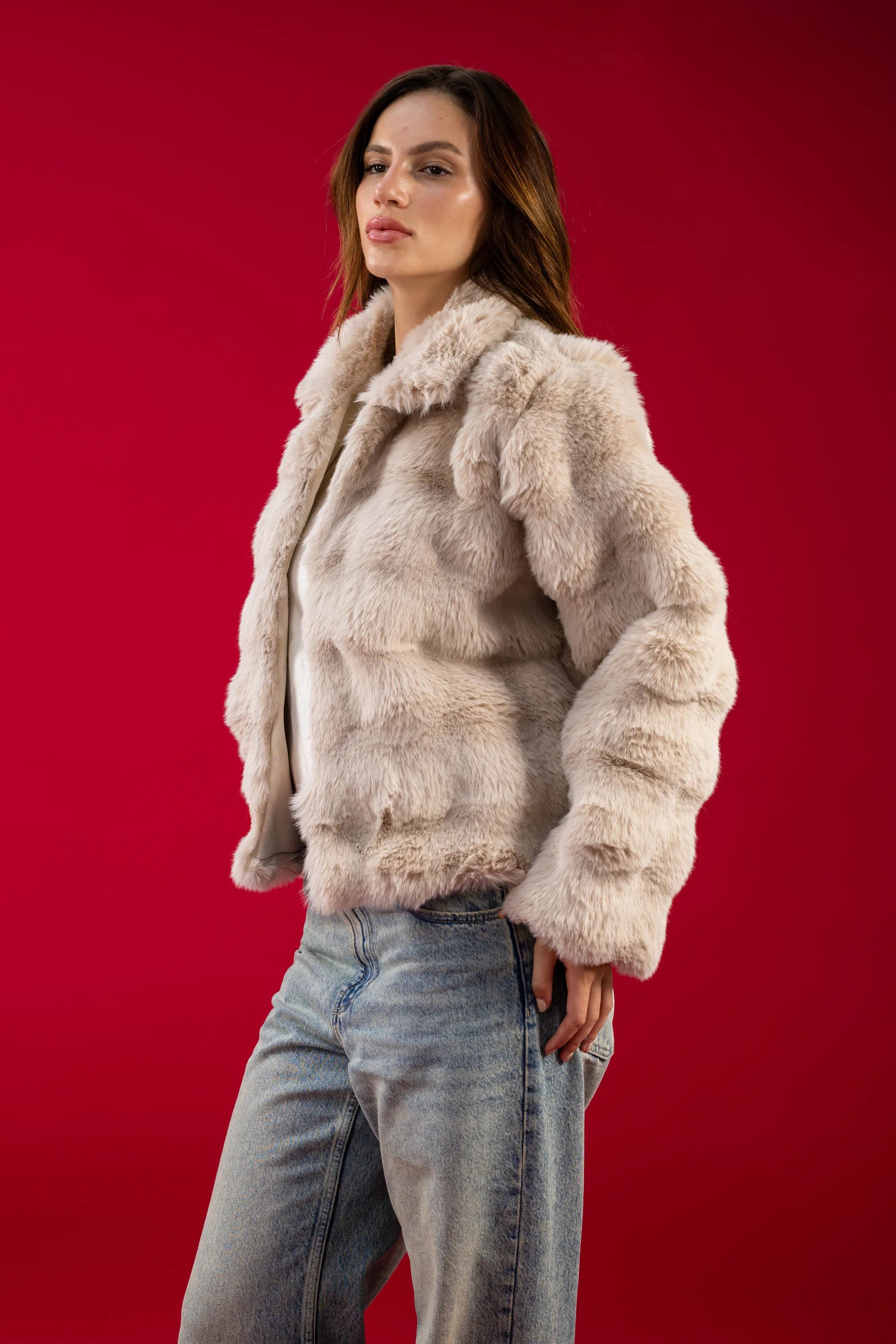 Woman wearing a beige fur jacket and jeans against a red background