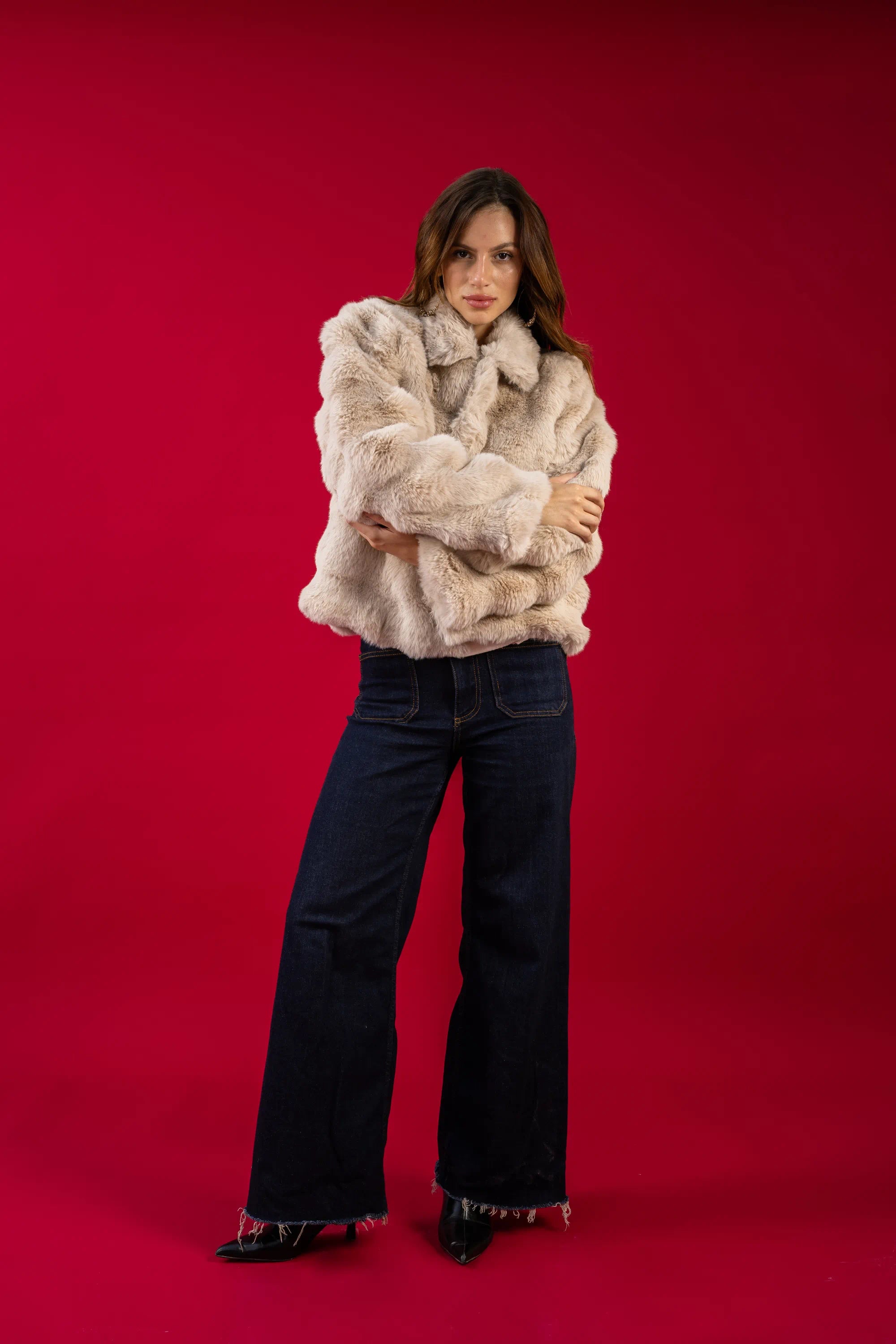 Woman wearing a fur coat and jeans against a red background