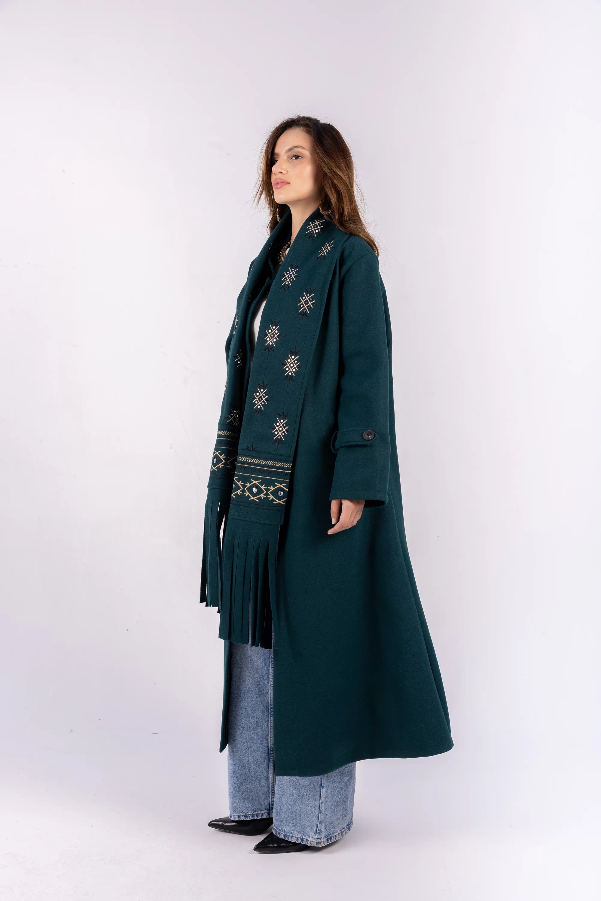 Woman wearing a long dark green coat with a patterned scarf on a white background