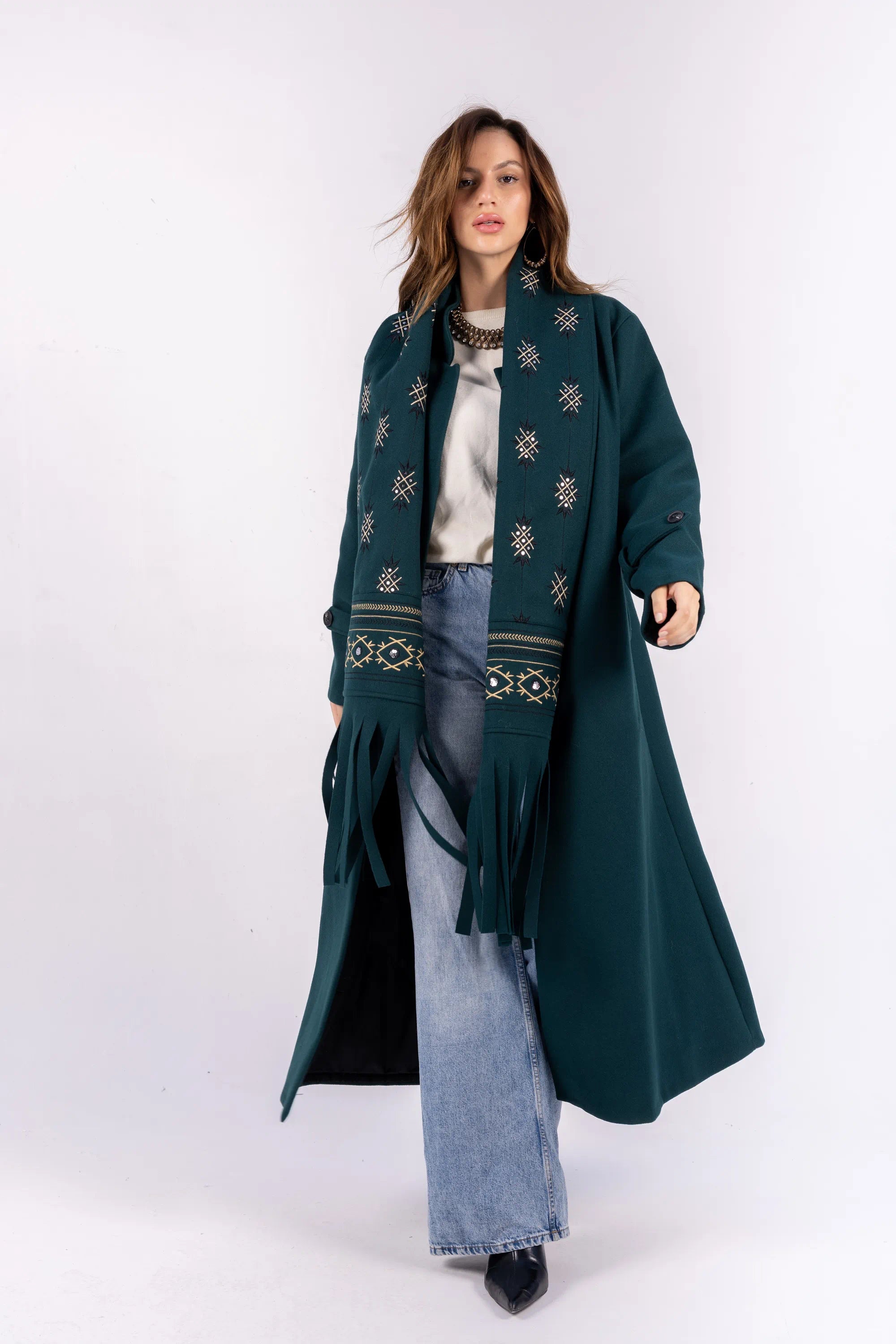 Woman wearing a long dark green coat with embroidery on a white background