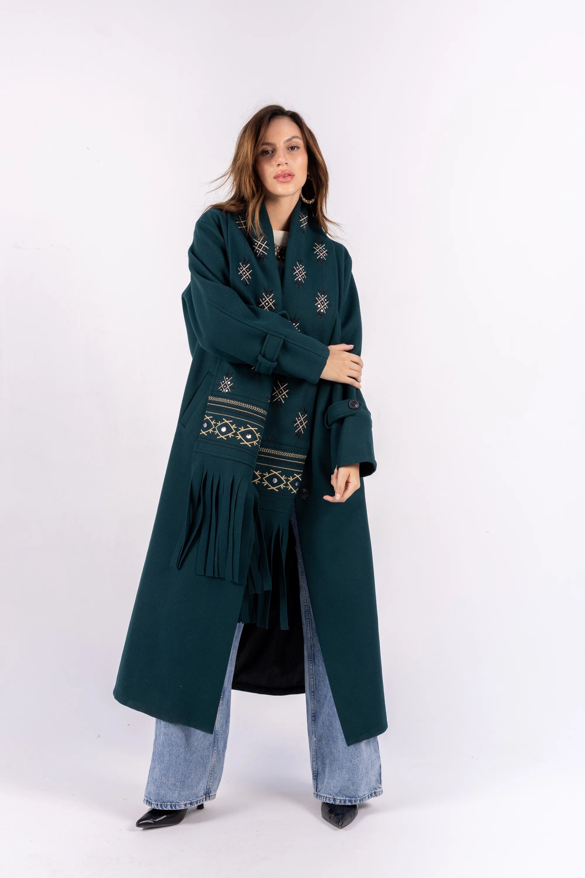Woman wearing a long dark green coat with embroidery on a white background