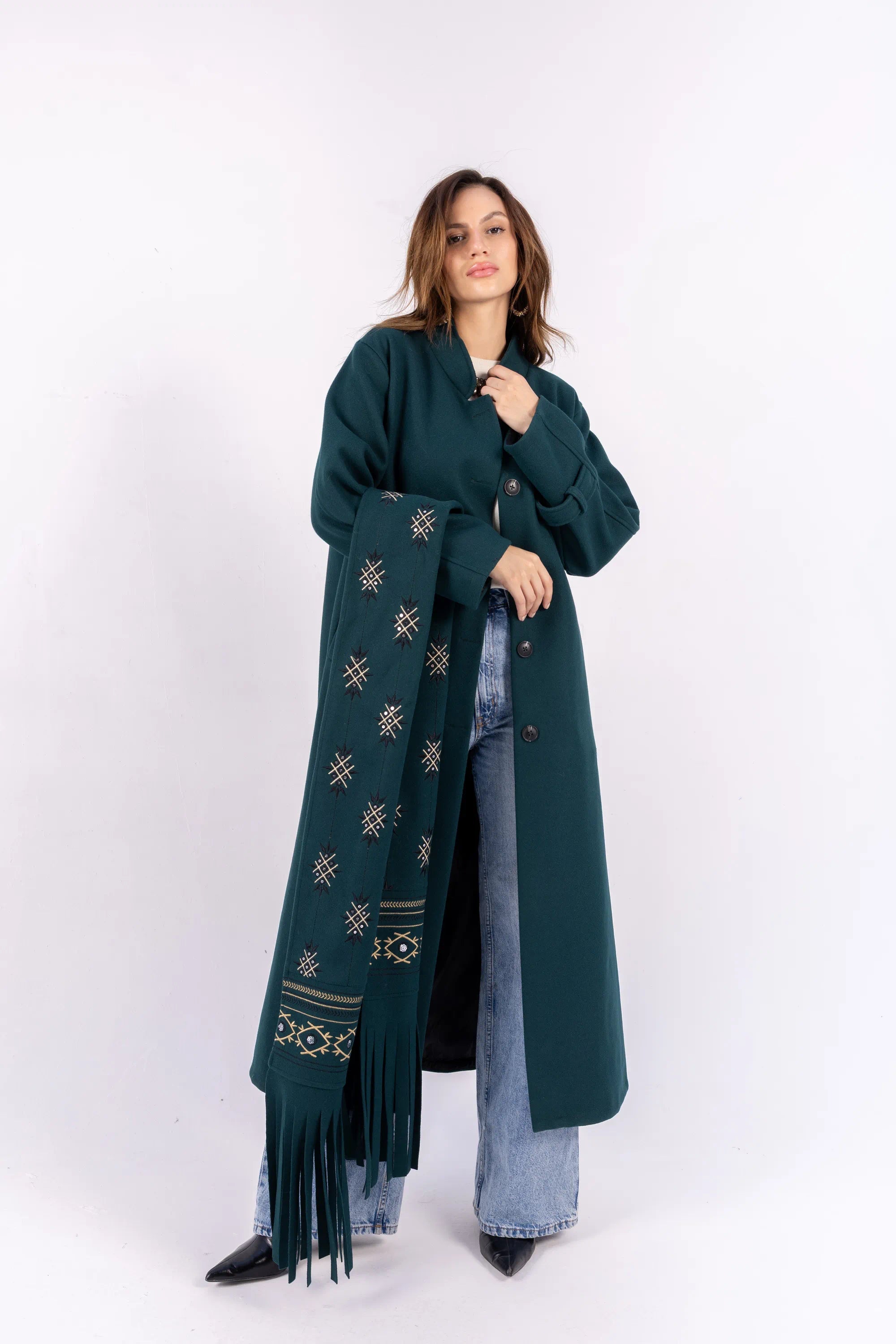 Woman wearing a long dark green coat with a patterned scarf on a white background