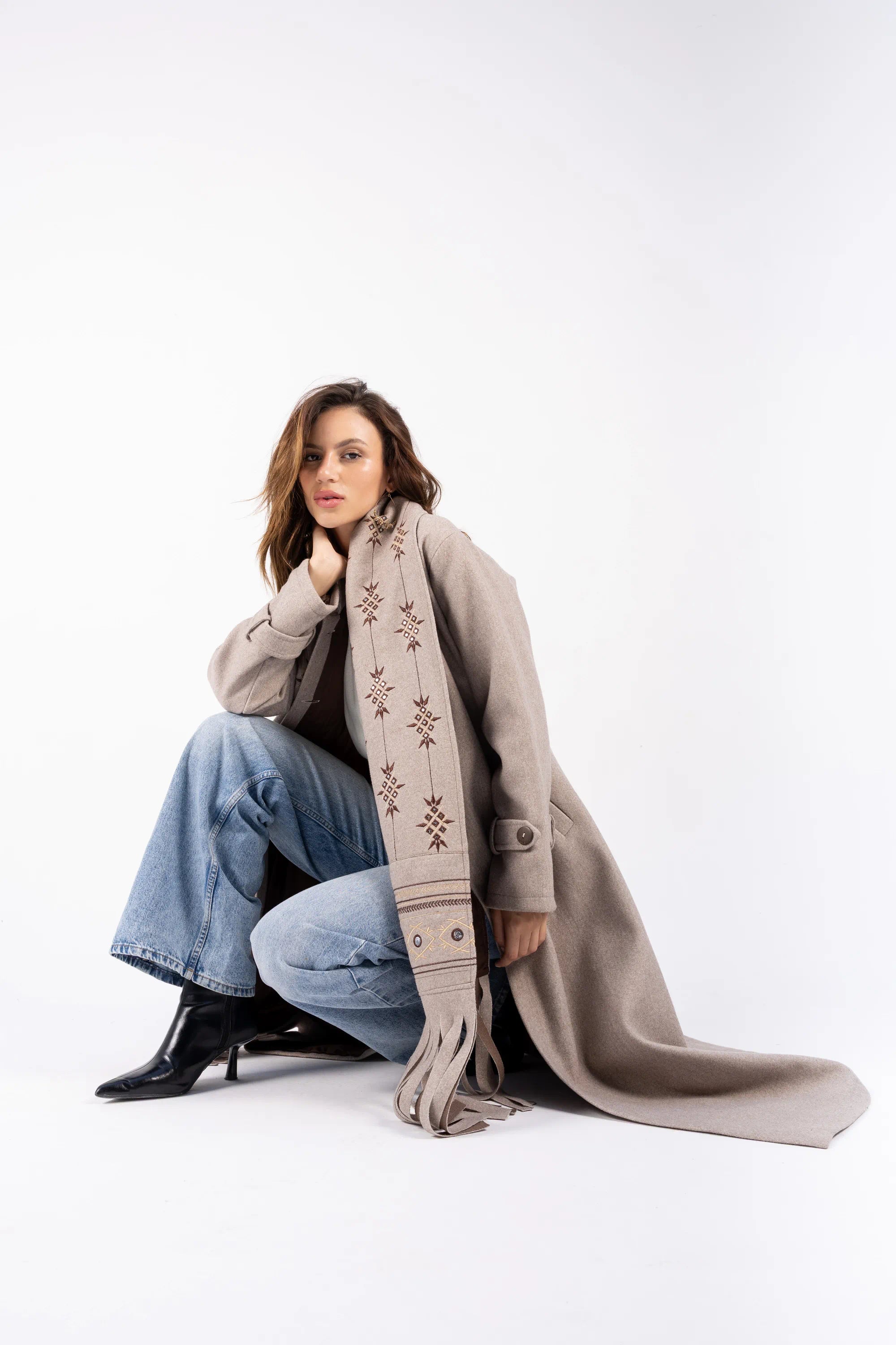 Woman wearing a long coat with a patterned scarf on a white background