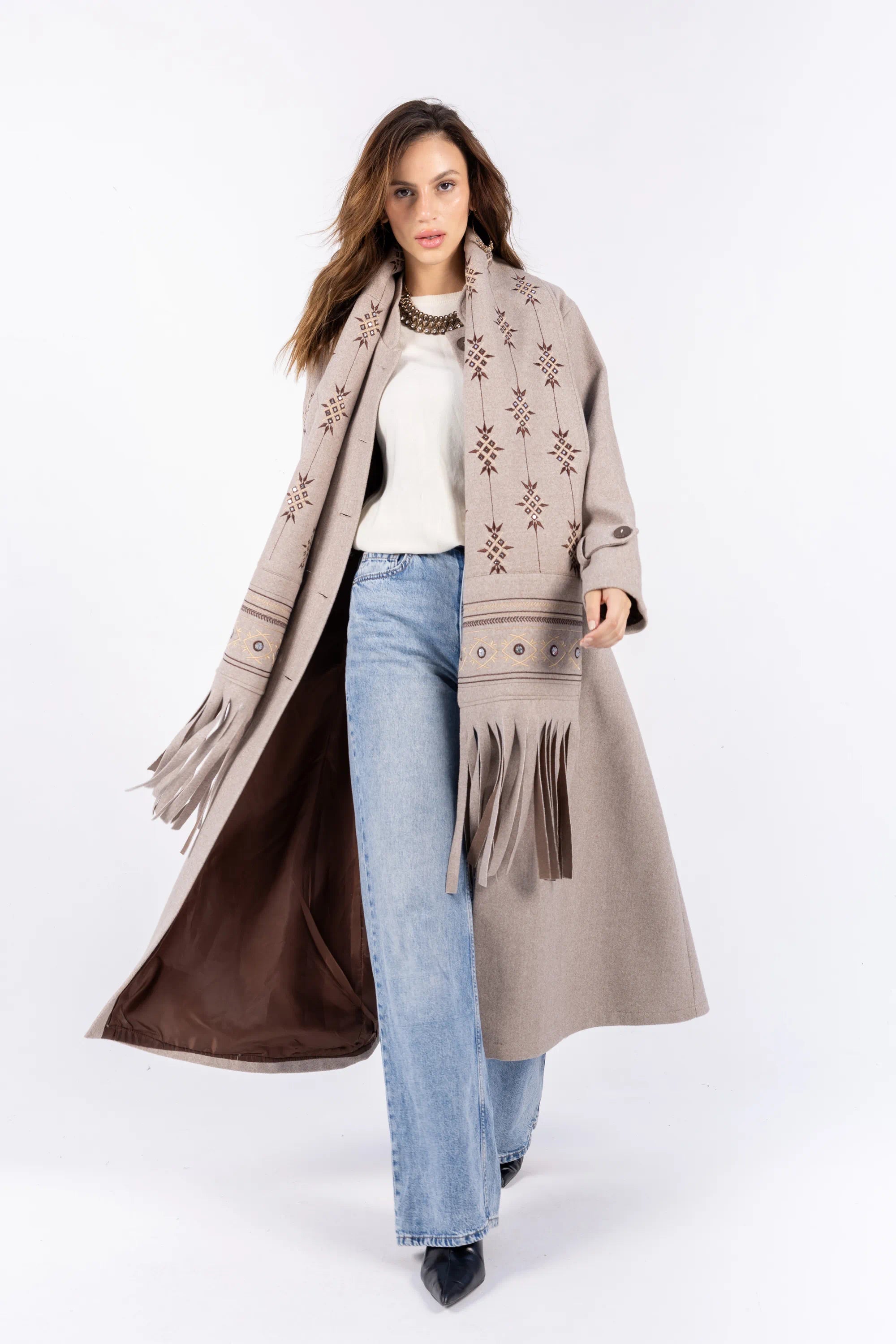 Woman wearing a long beige coat with a patterned scarf on a white background