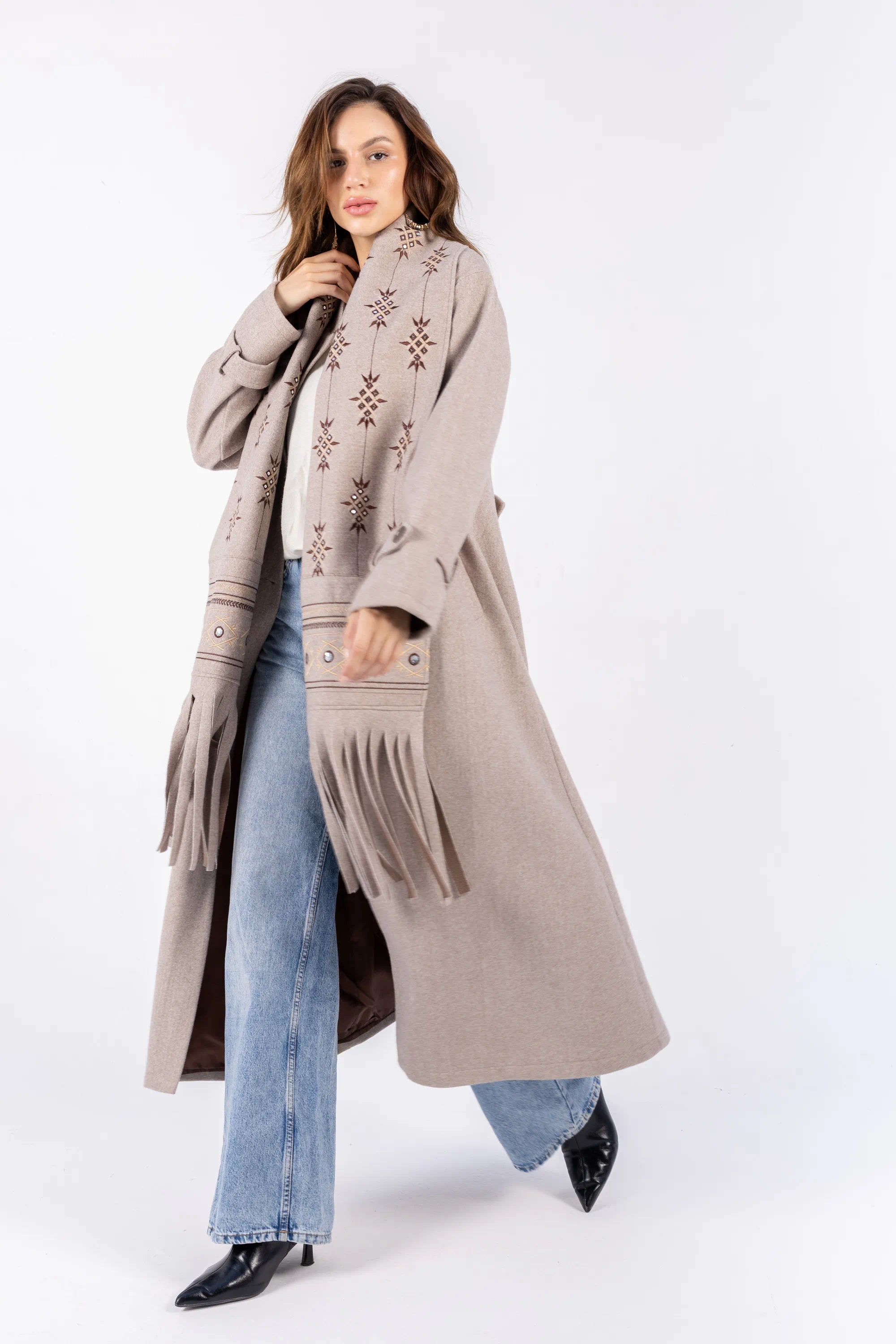Woman wearing a long beige coat with a patterned sweater and jeans on a white background