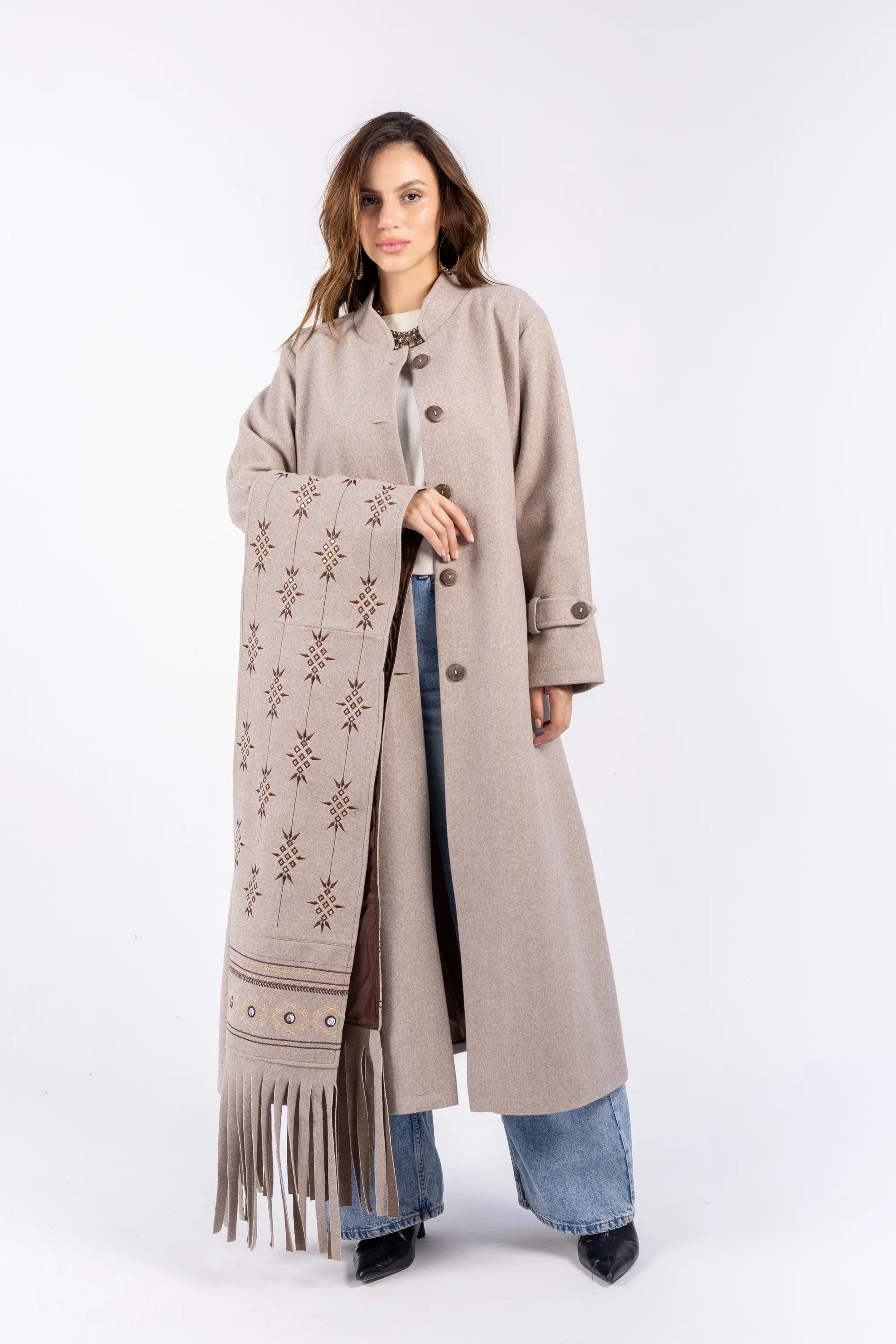 Woman wearing a long beige coat with a patterned scarf on a white background