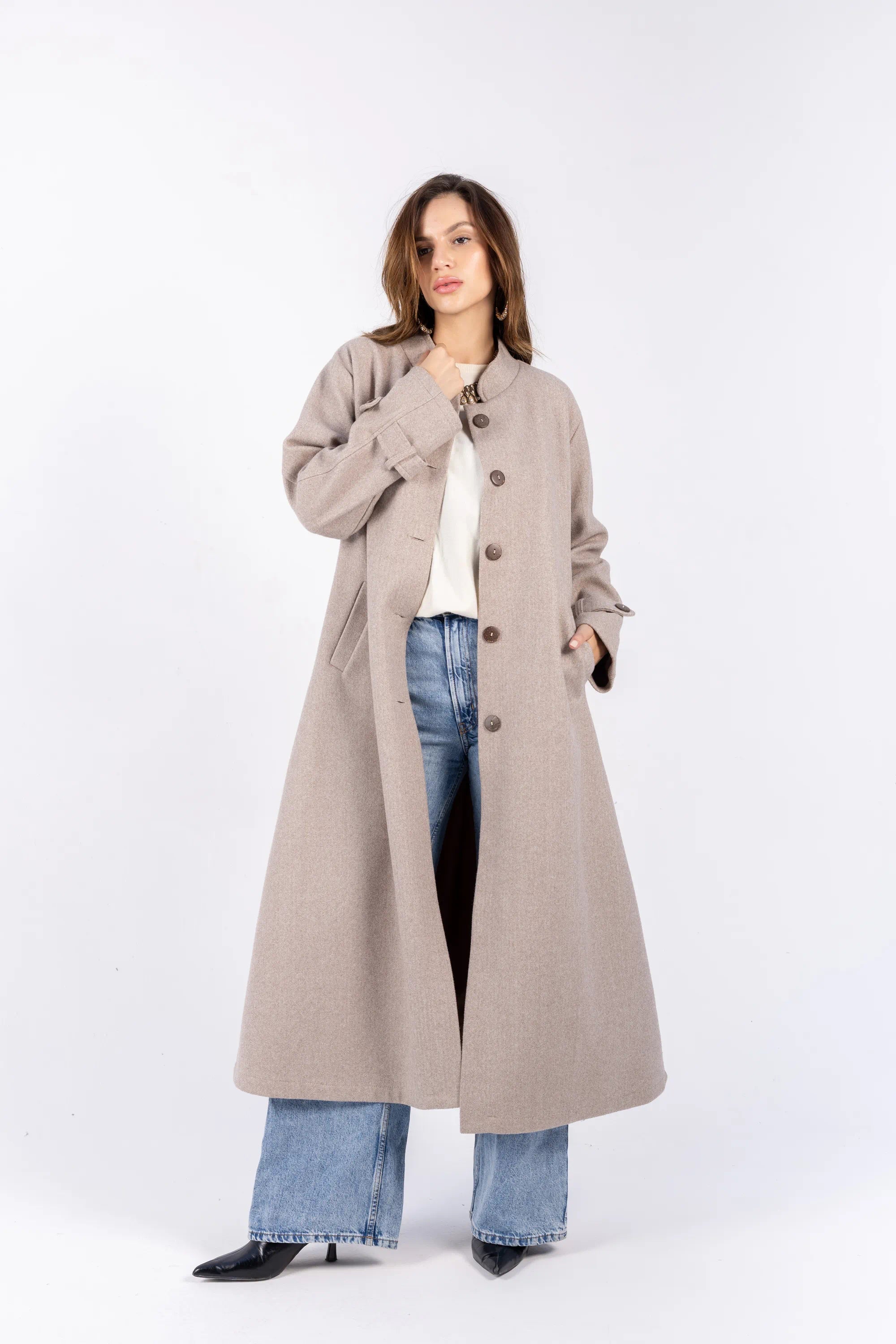 Woman wearing a long beige coat over jeans on a white background
