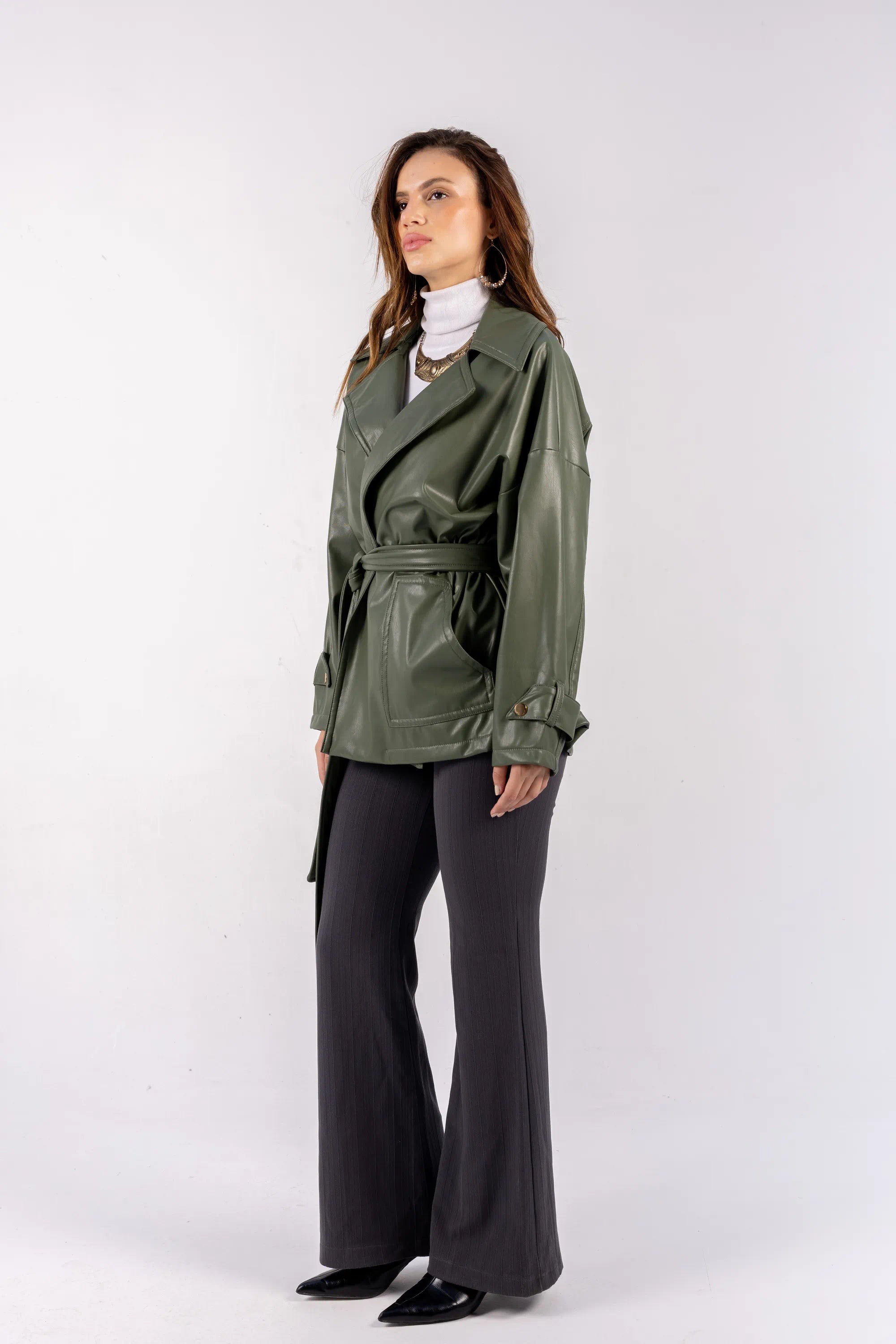 Woman wearing a green trench coat and gray pants on a white background