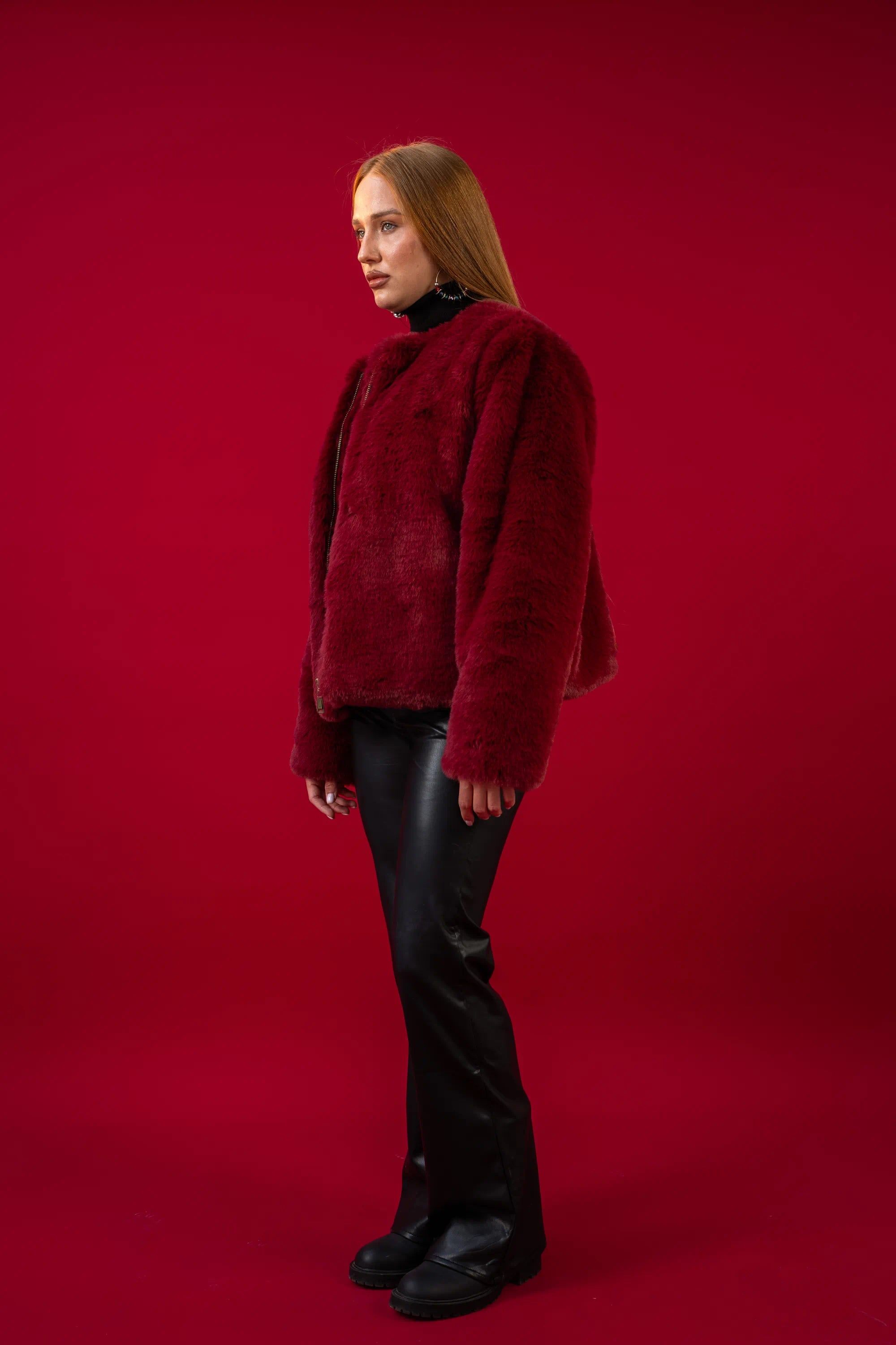 Person wearing a red textured sweater and black pants on a red background