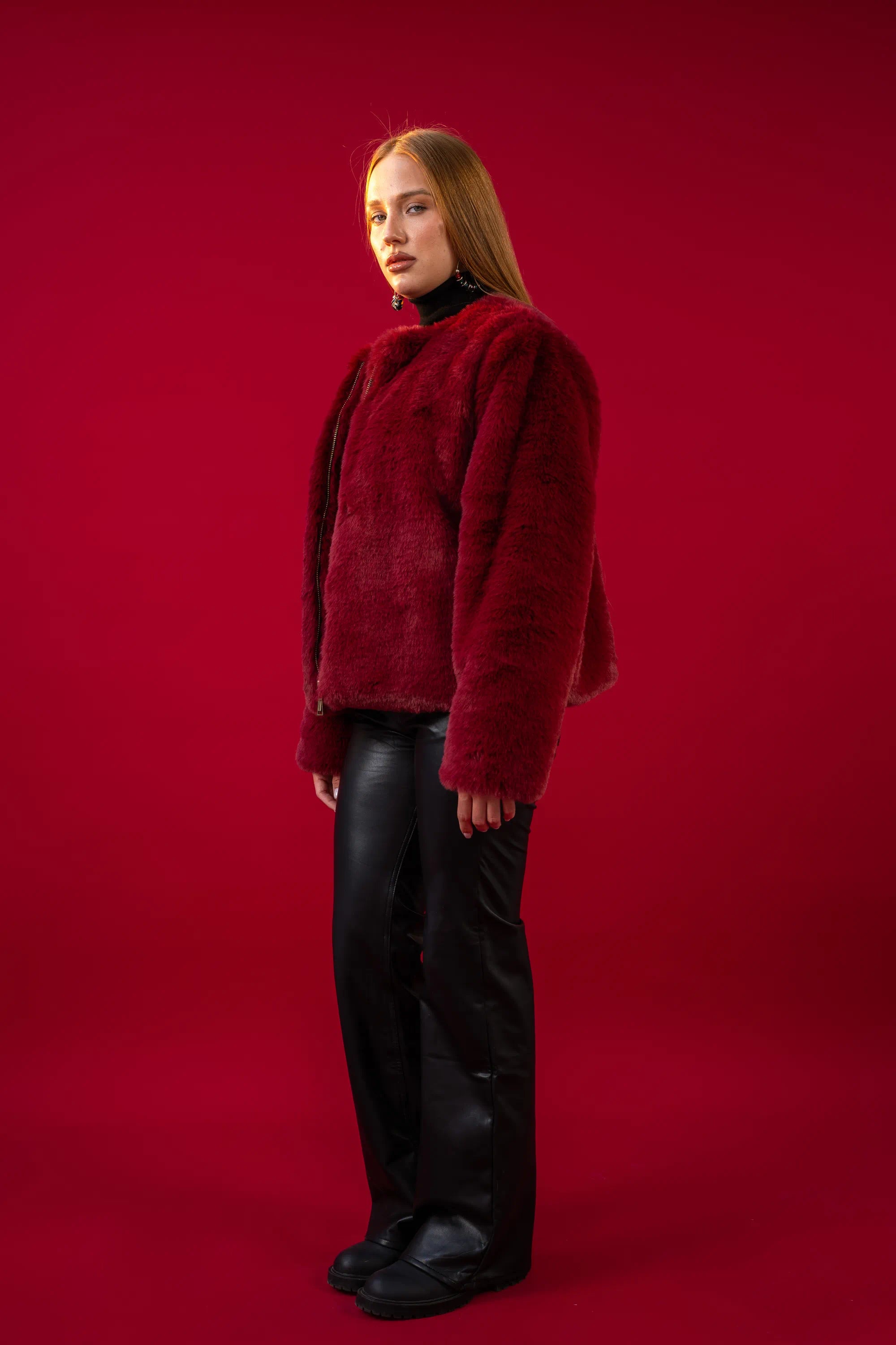 Person wearing a red fluffy sweater and black pants on a red background