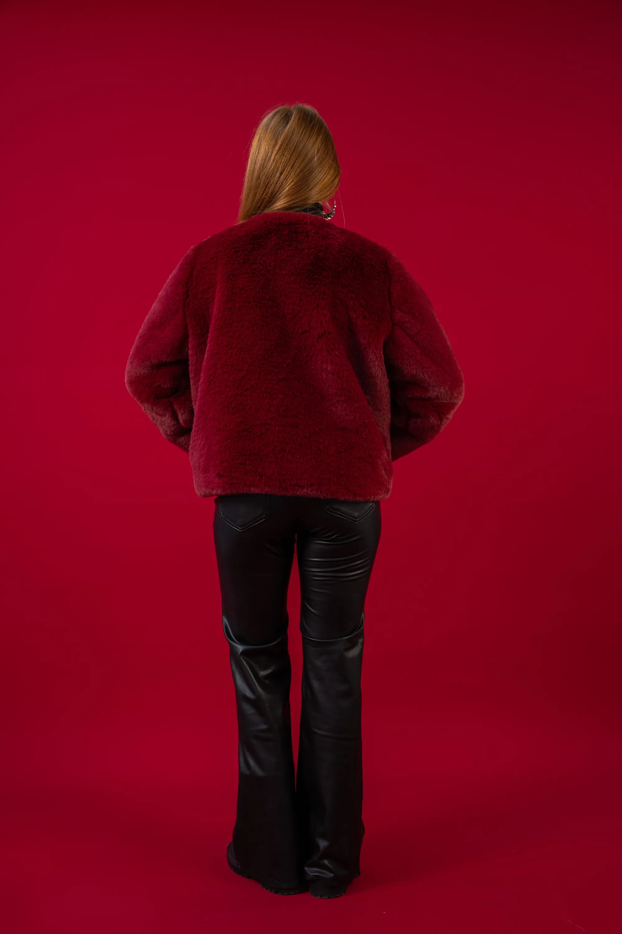 Person wearing a red jacket and black pants on a red background