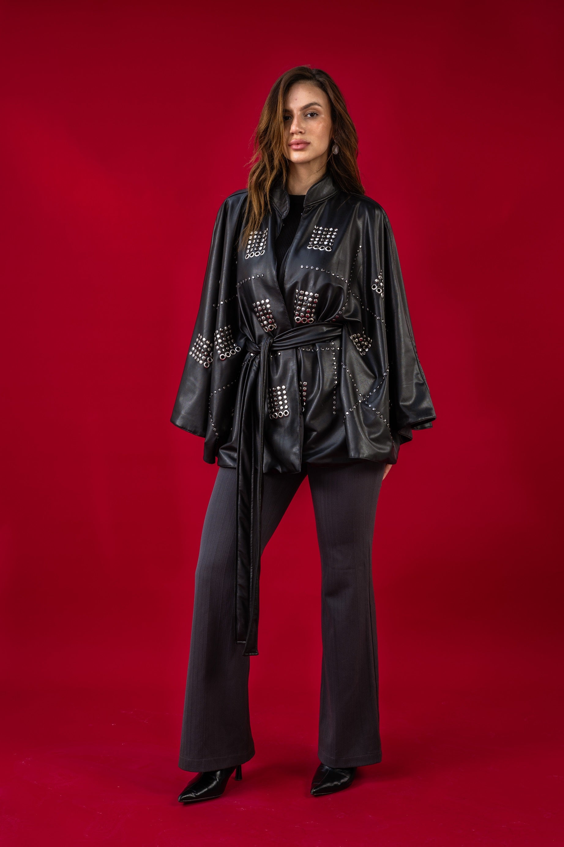 Woman wearing a black outfit with studded details on a red background