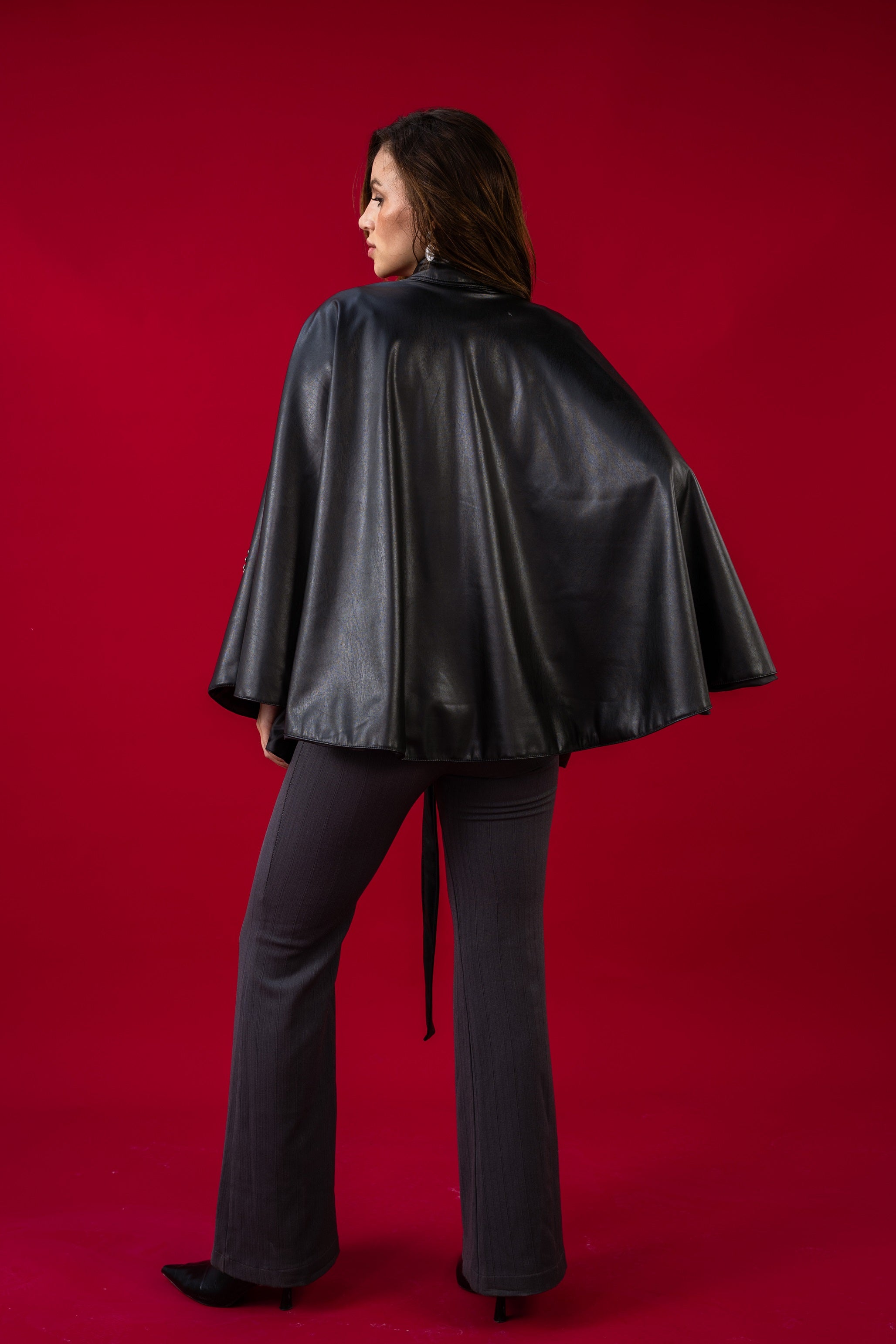 Person wearing a black leather cape against a red background