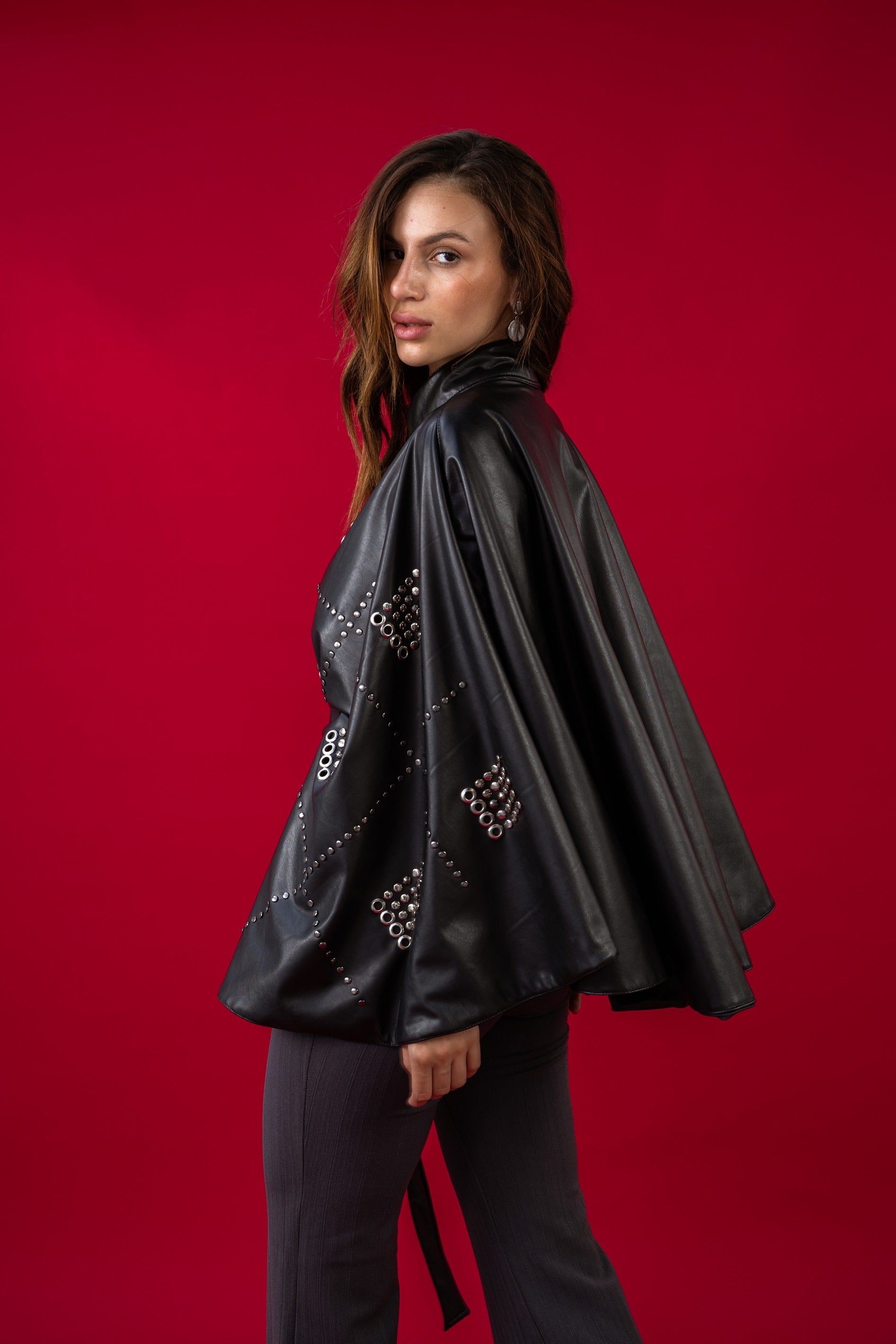 Woman wearing a black leather outfit with studs on a red background