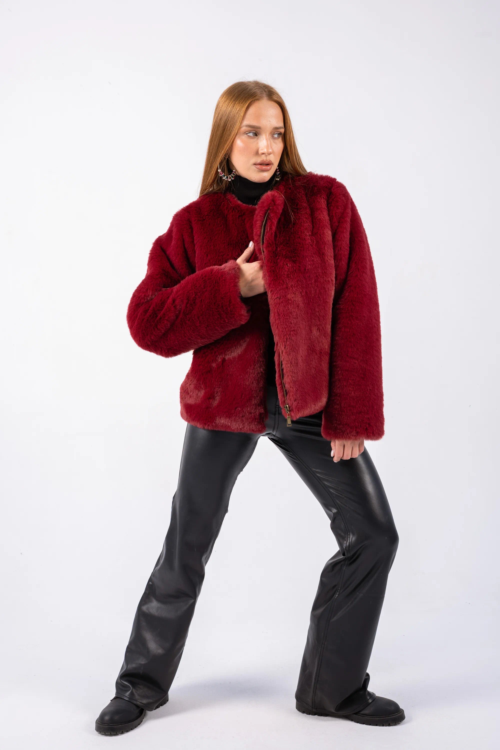 Person wearing a red fur coat and black pants on a white background