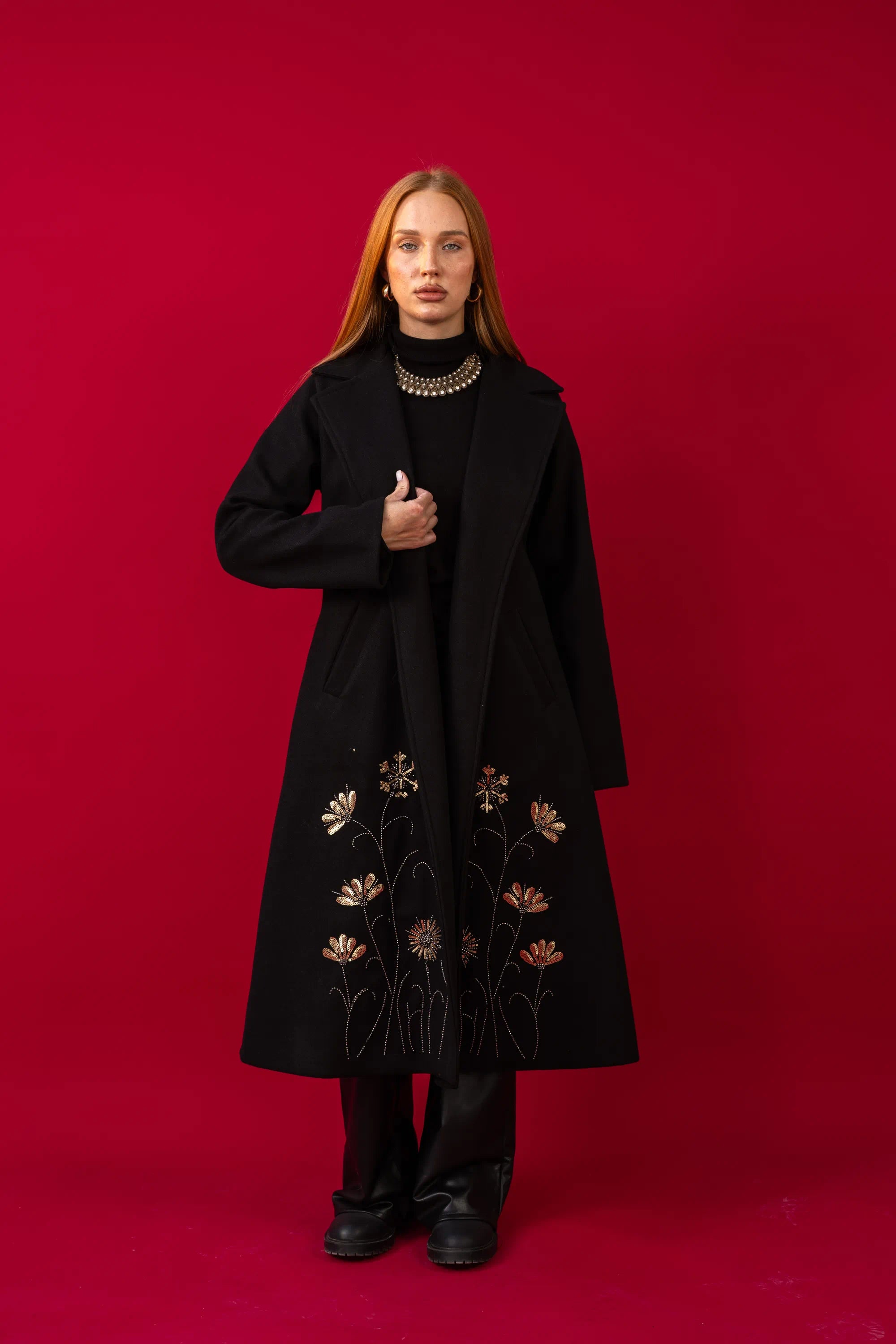 Person wearing a black coat with floral embroidery on a red background