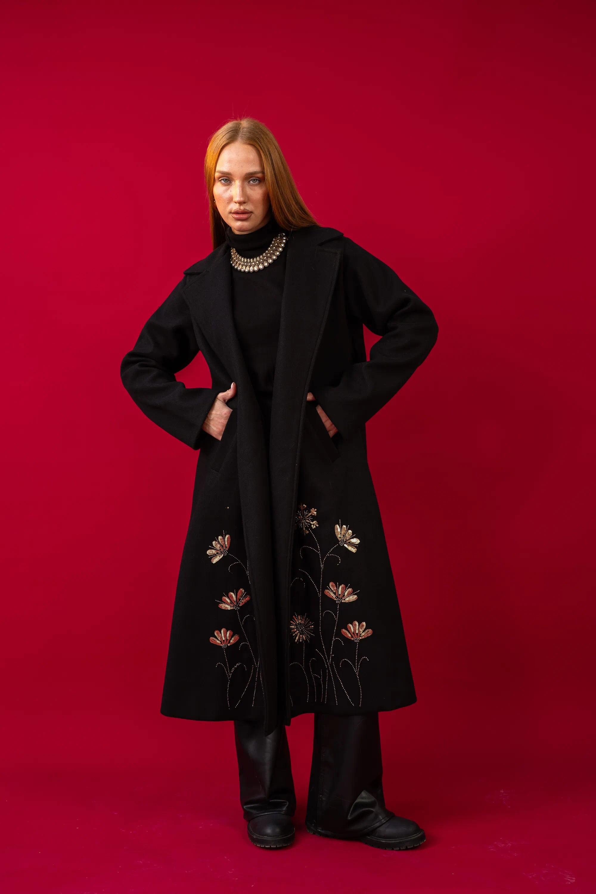 Woman wearing a black coat with floral embroidery on a red background