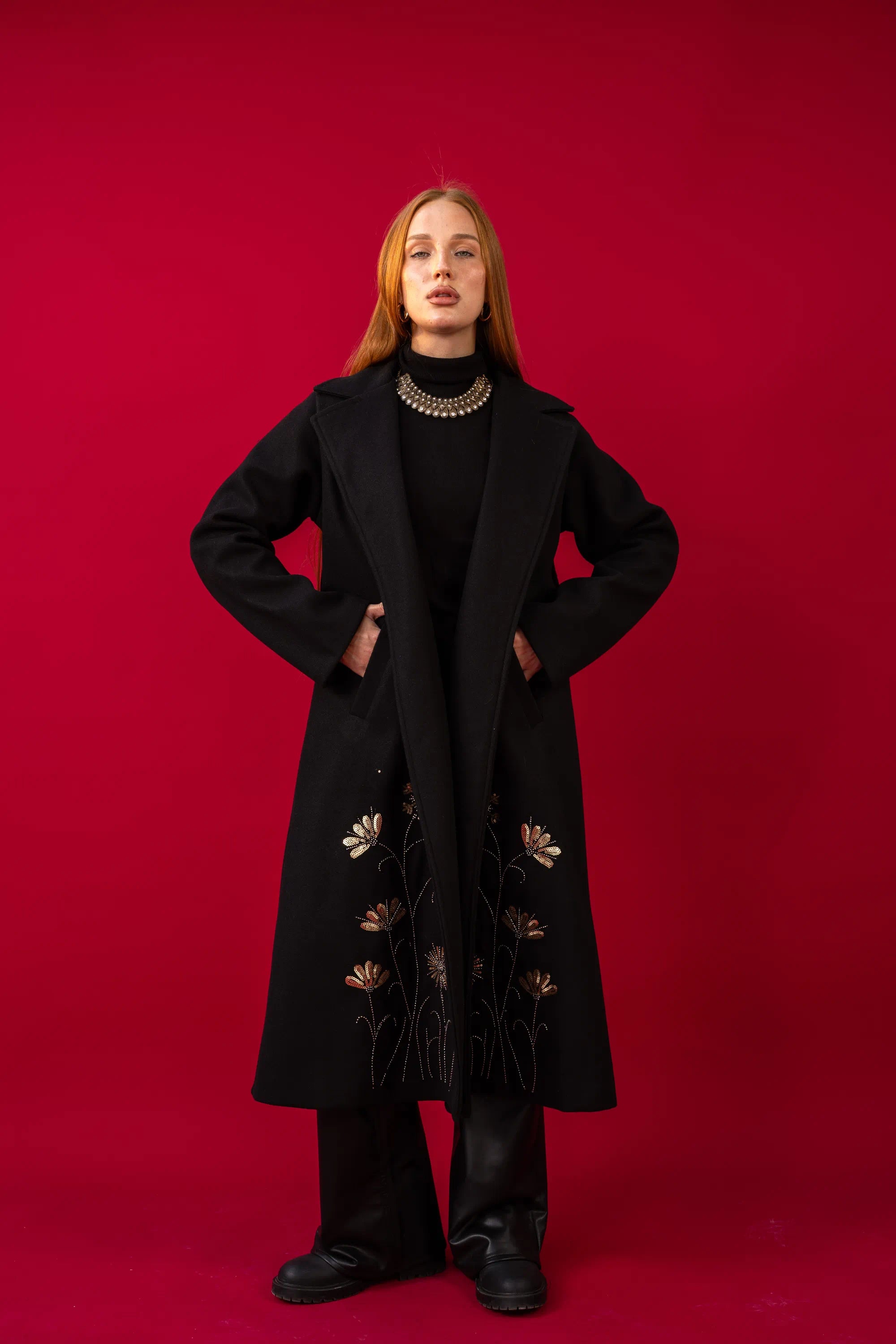 Person wearing a black coat with gold embroidery on a red background