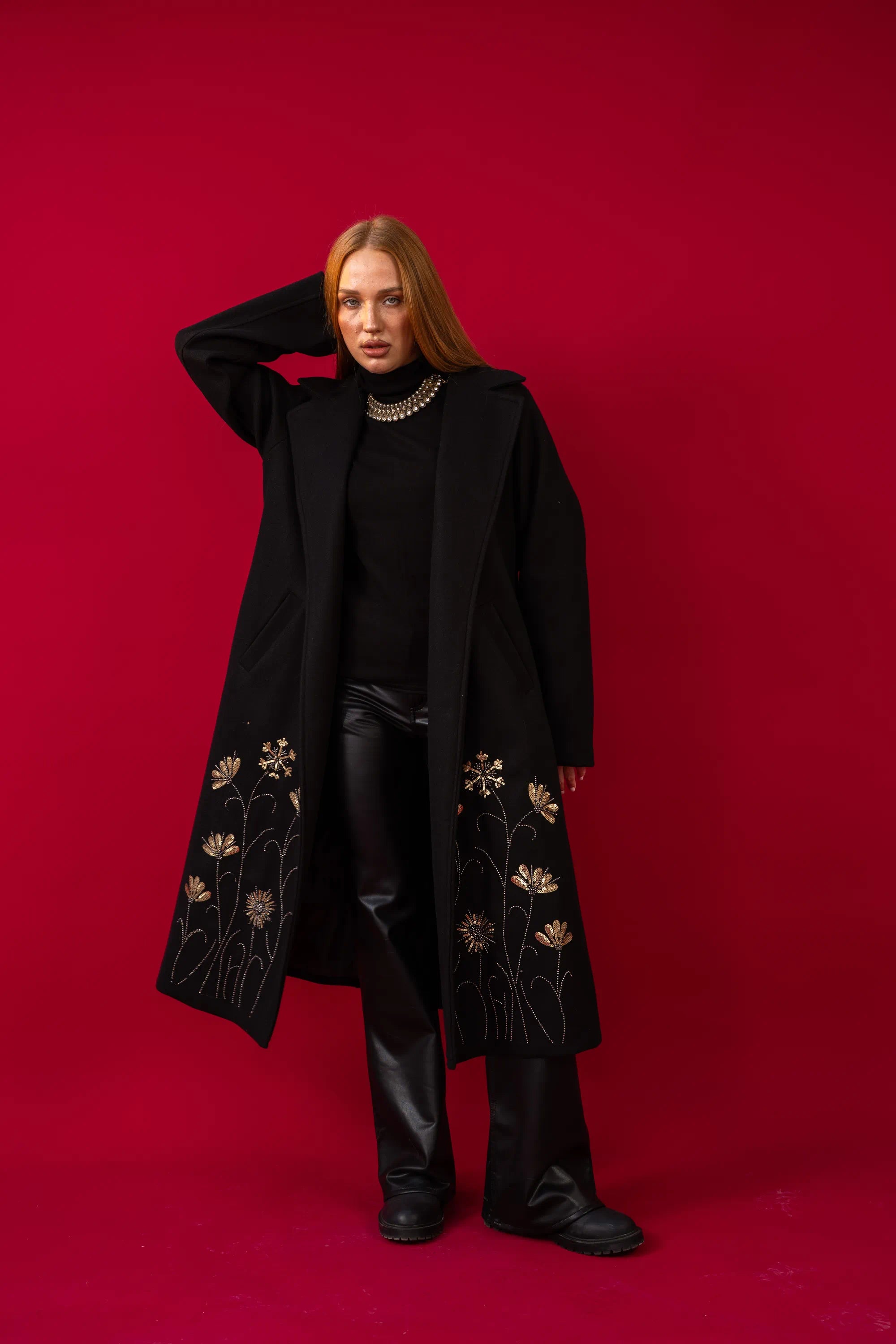 Person wearing a black coat with floral embroidery on a red background