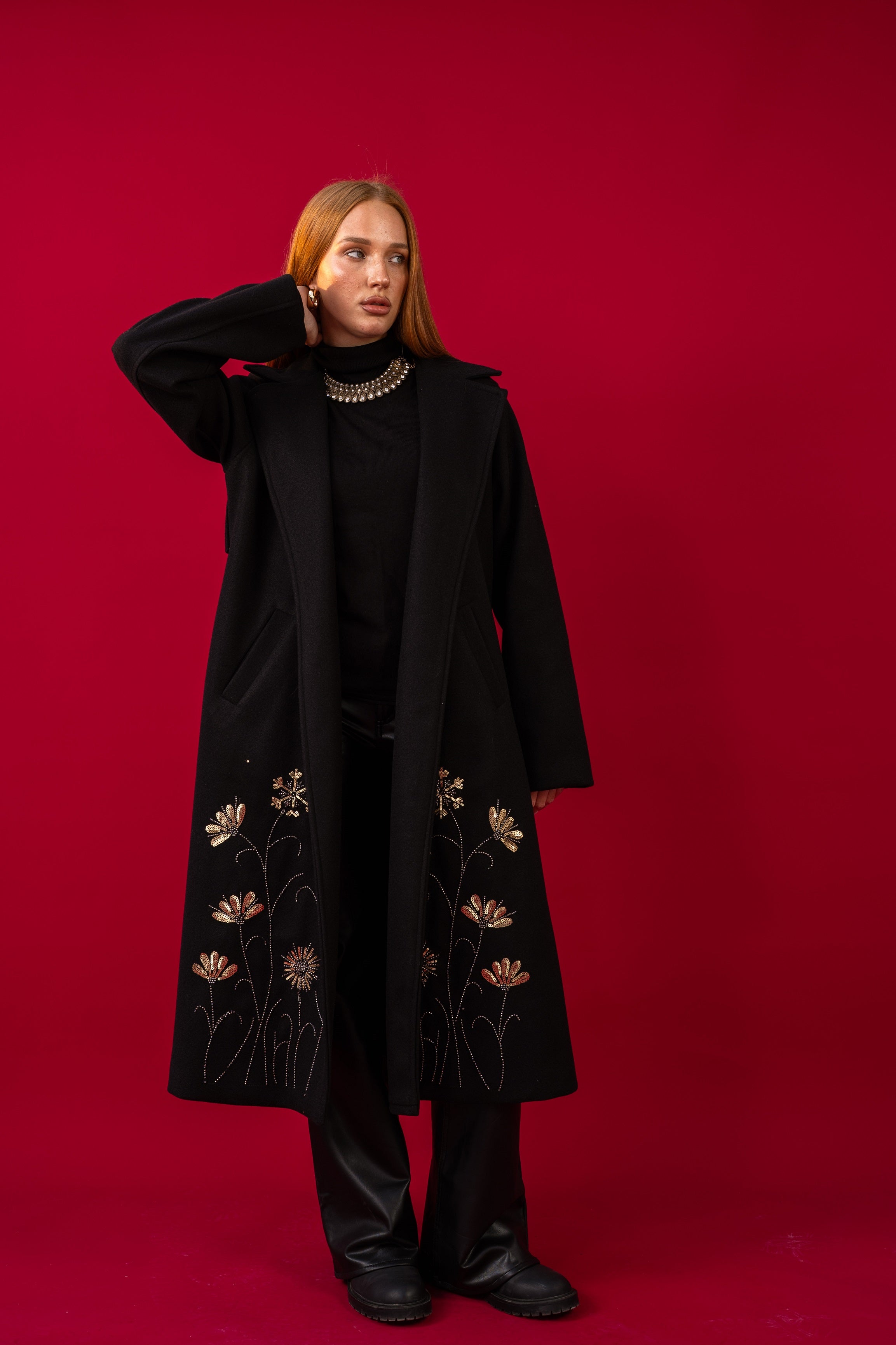 Person wearing a black coat with floral embroidery on a red background