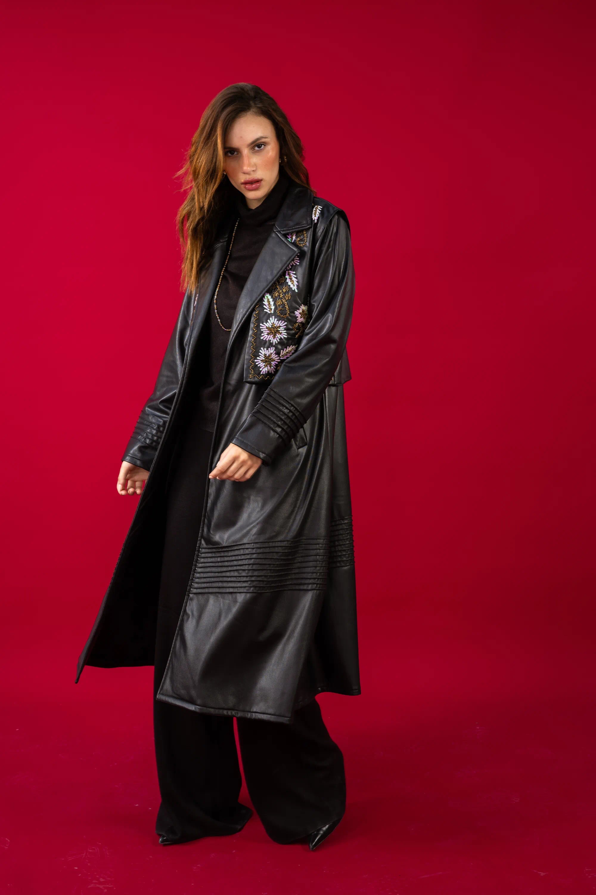 Woman wearing a long black coat with floral embroidery on a red background