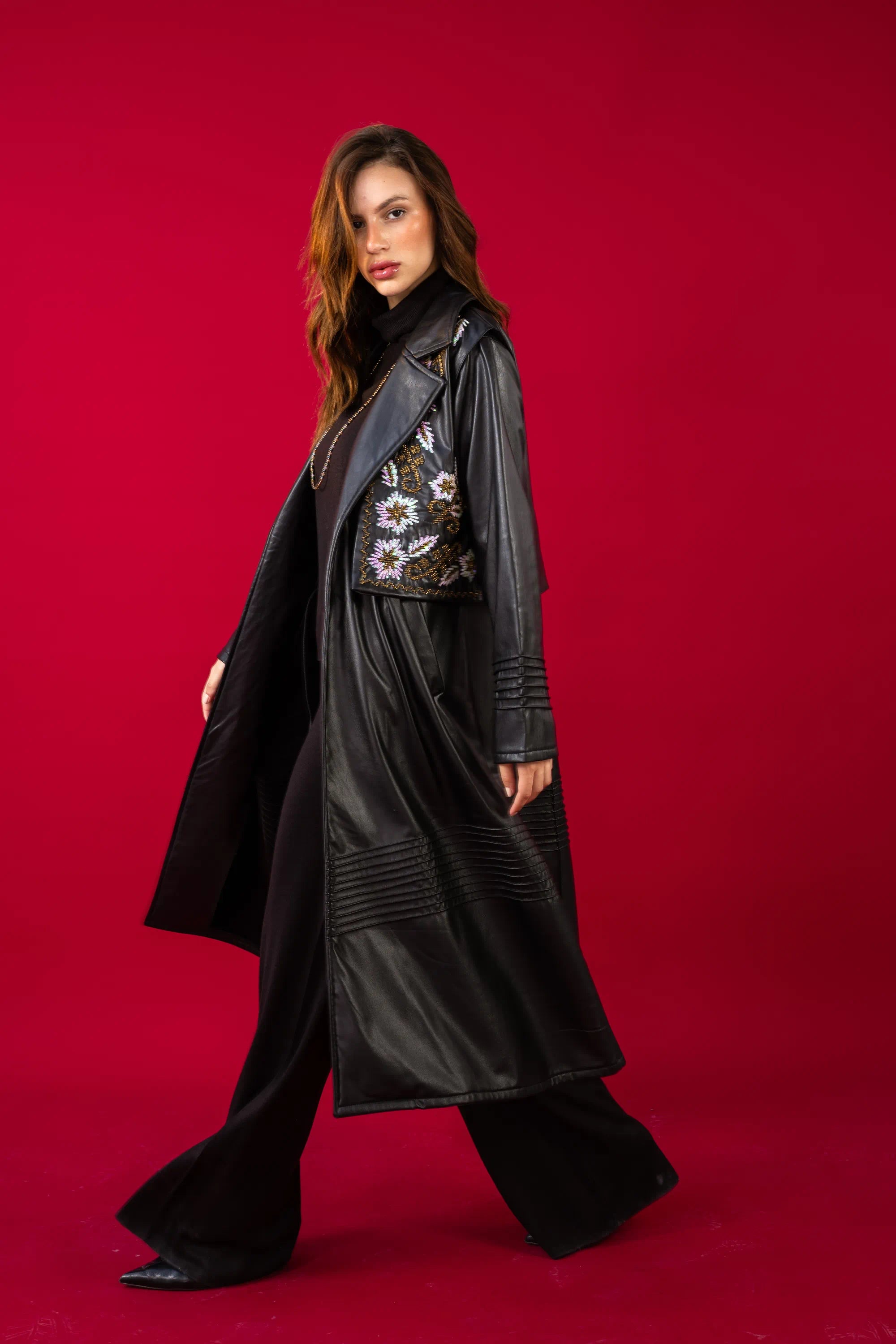 Woman wearing a long black coat with floral embroidery on a red background