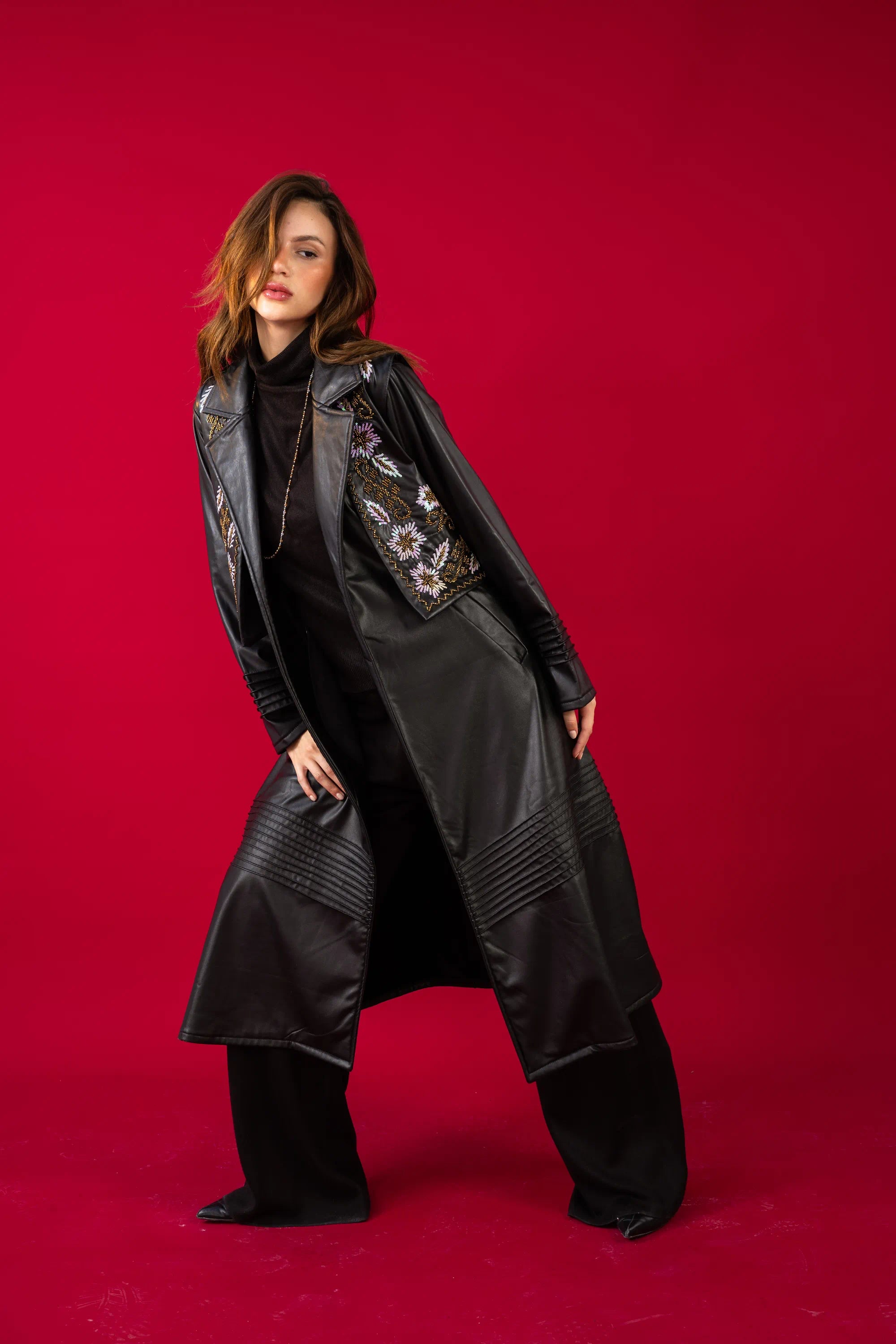 Woman wearing a long black coat with floral embroidery on a red background