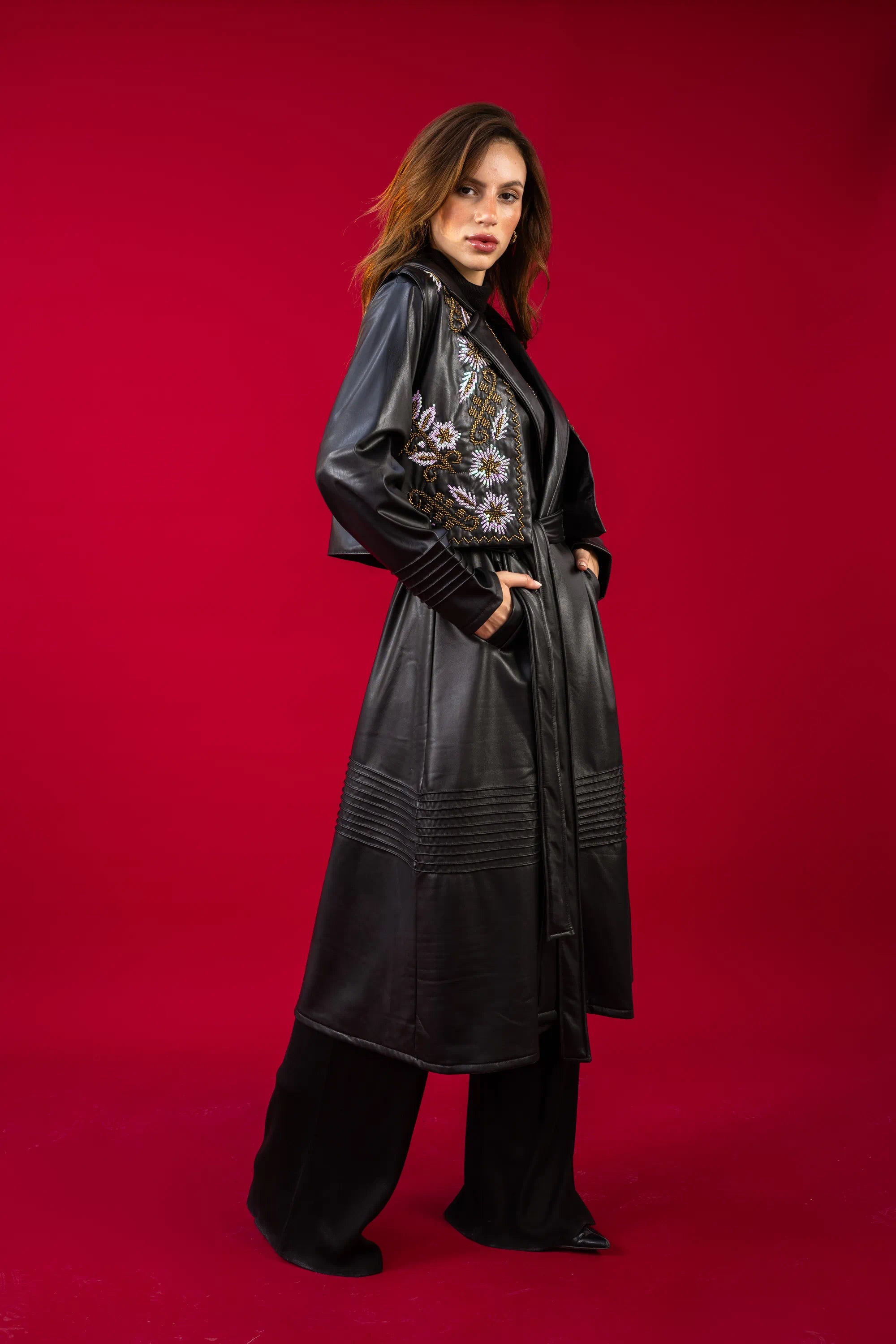Woman wearing a long black coat with floral embroidery on a red background