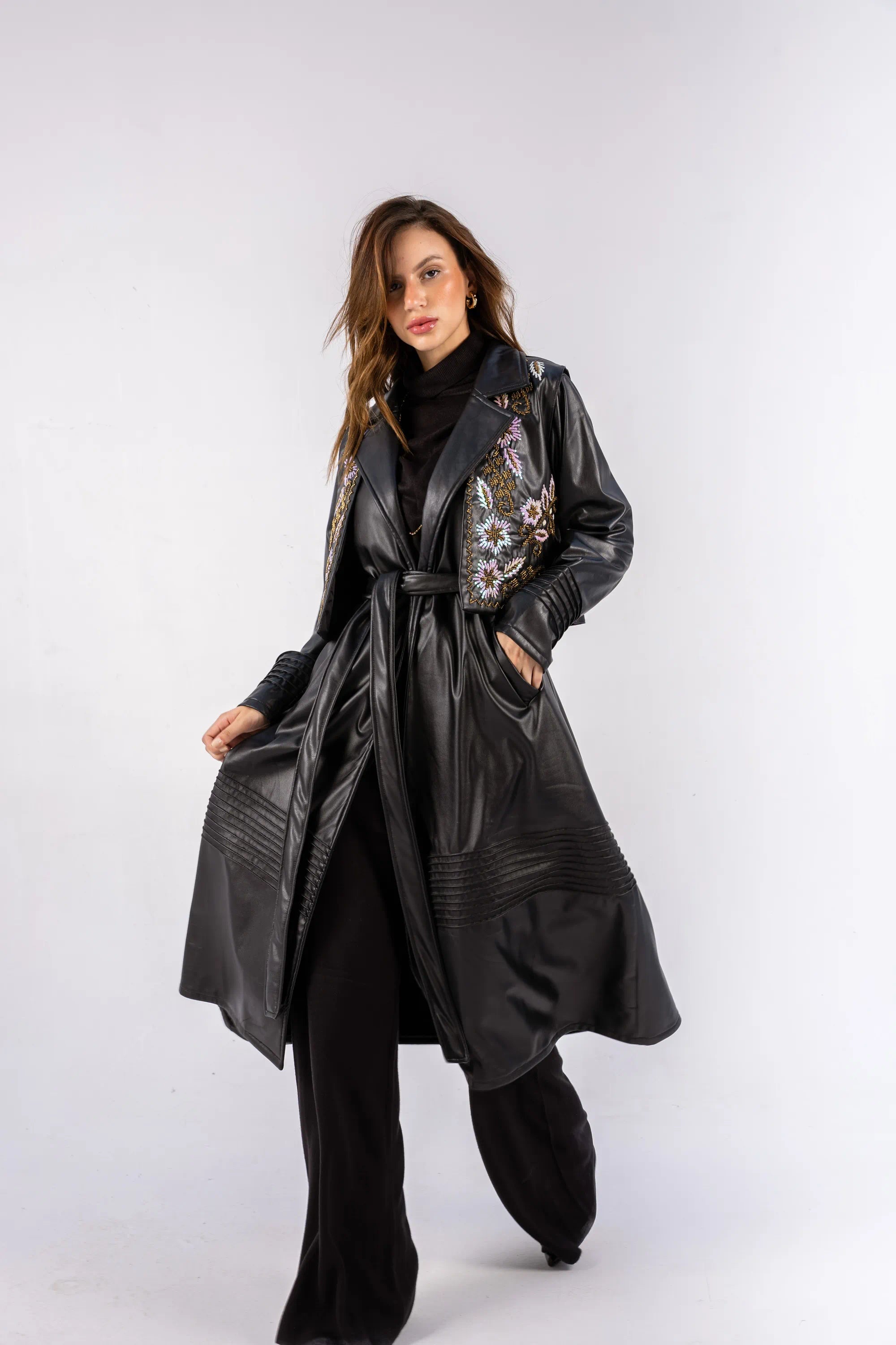 Woman wearing a black leather coat with floral embroidery on a white background