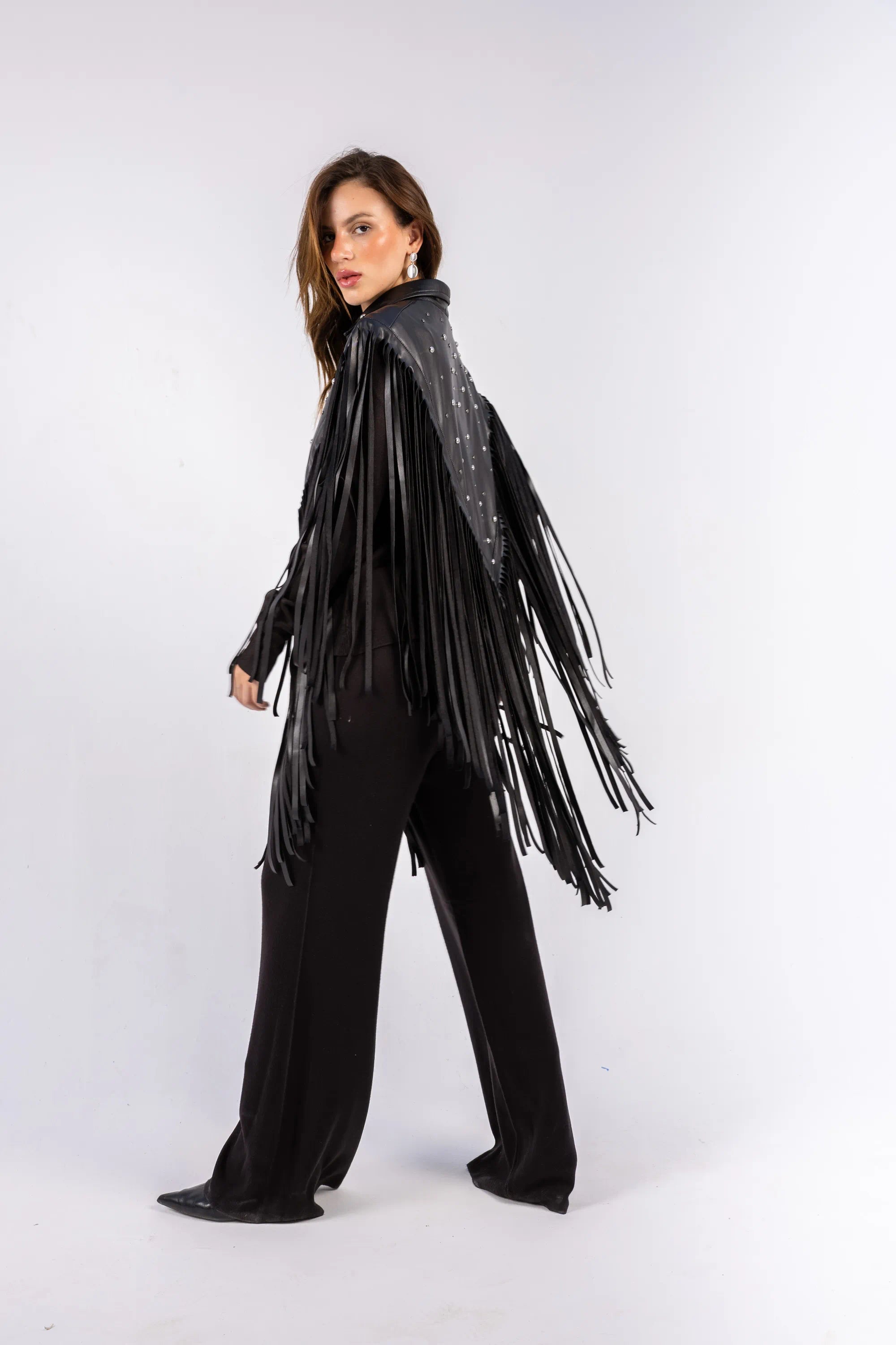 Woman wearing a black fringe jacket and pants on a white background