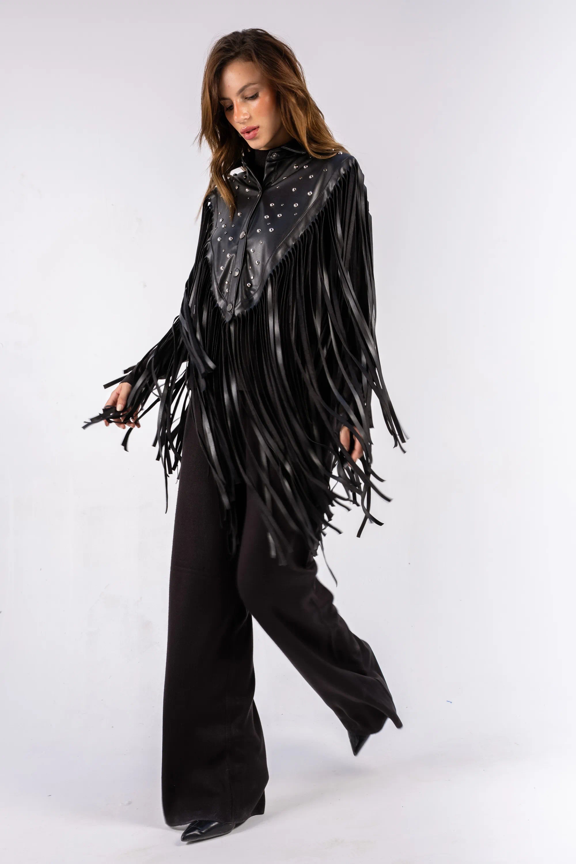 Woman wearing a black leather fringe poncho with a studded collar on a white background