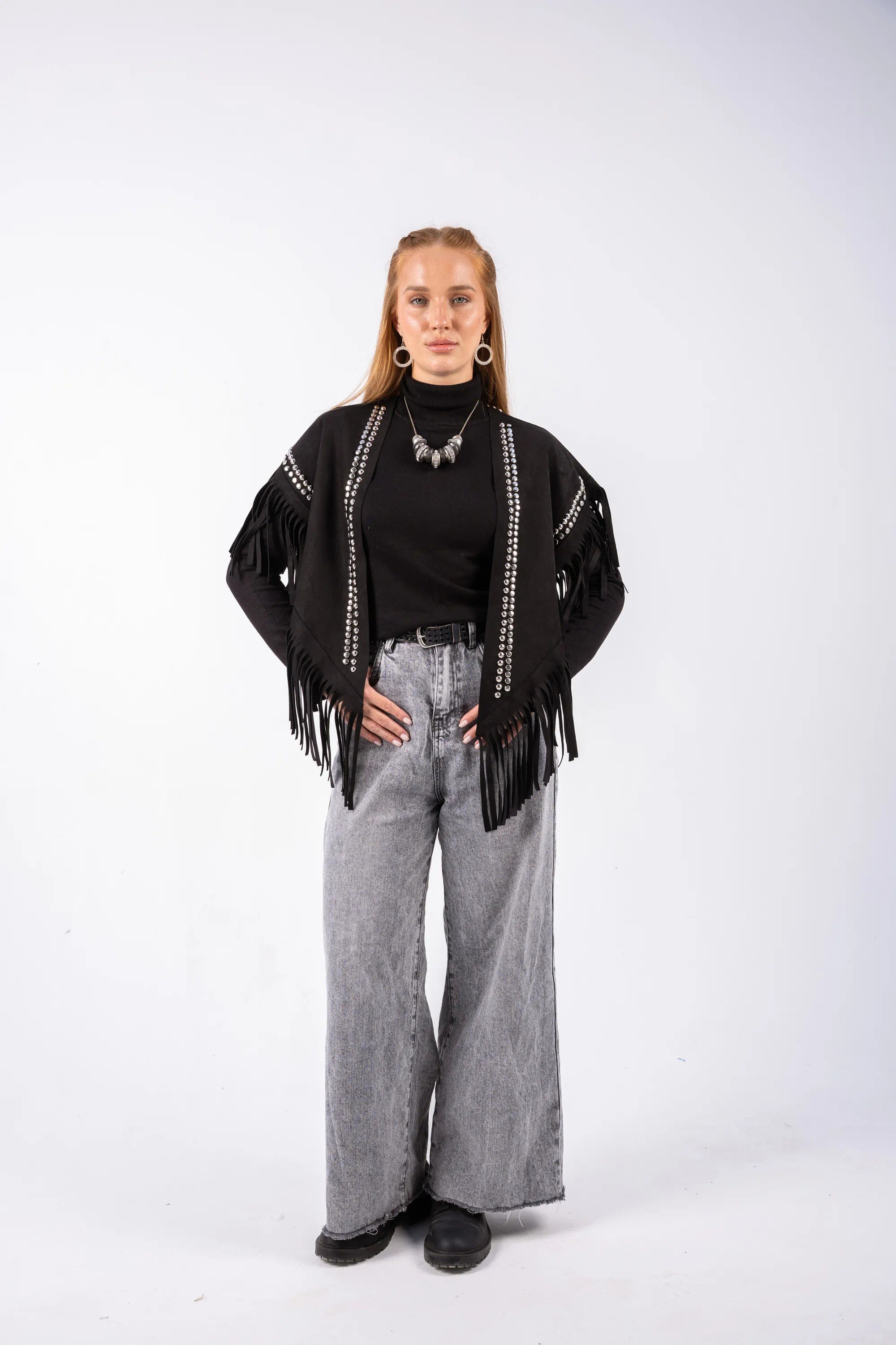 Person wearing a black top with fringe and gray pants on a white background