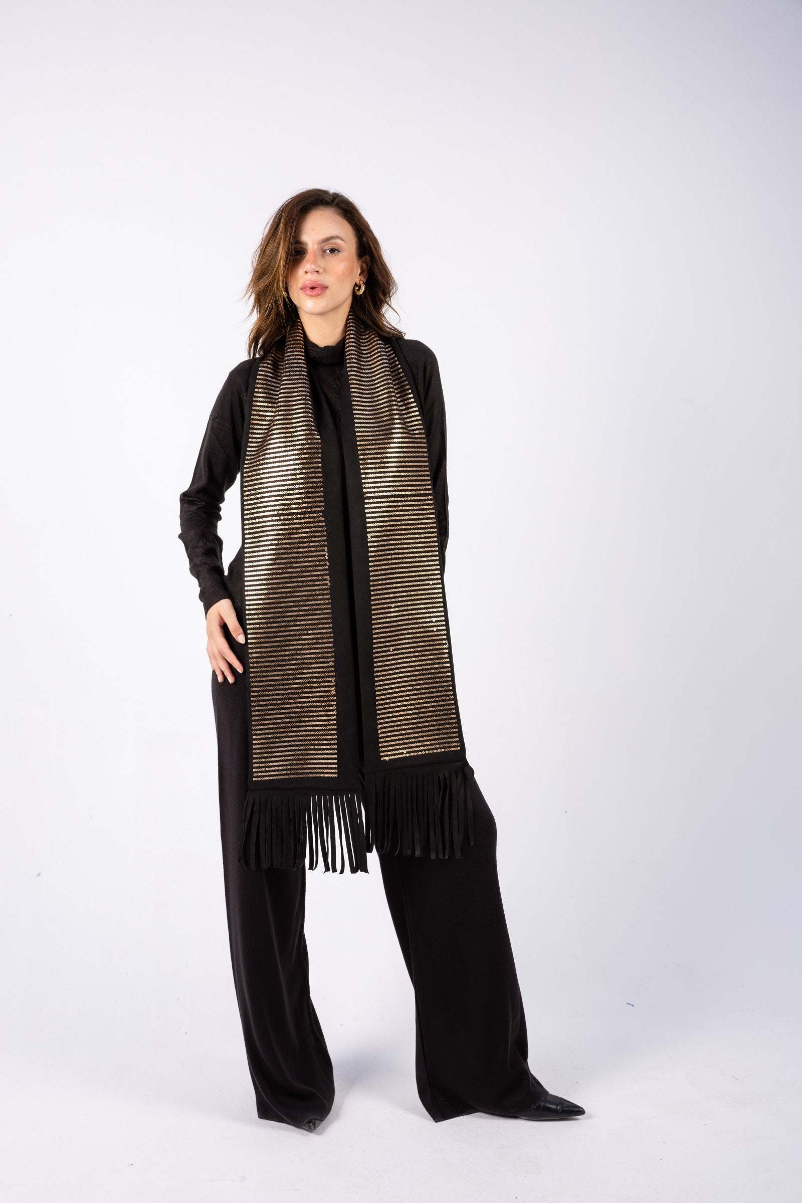 Woman wearing a long, patterned scarf with fringe on a white background