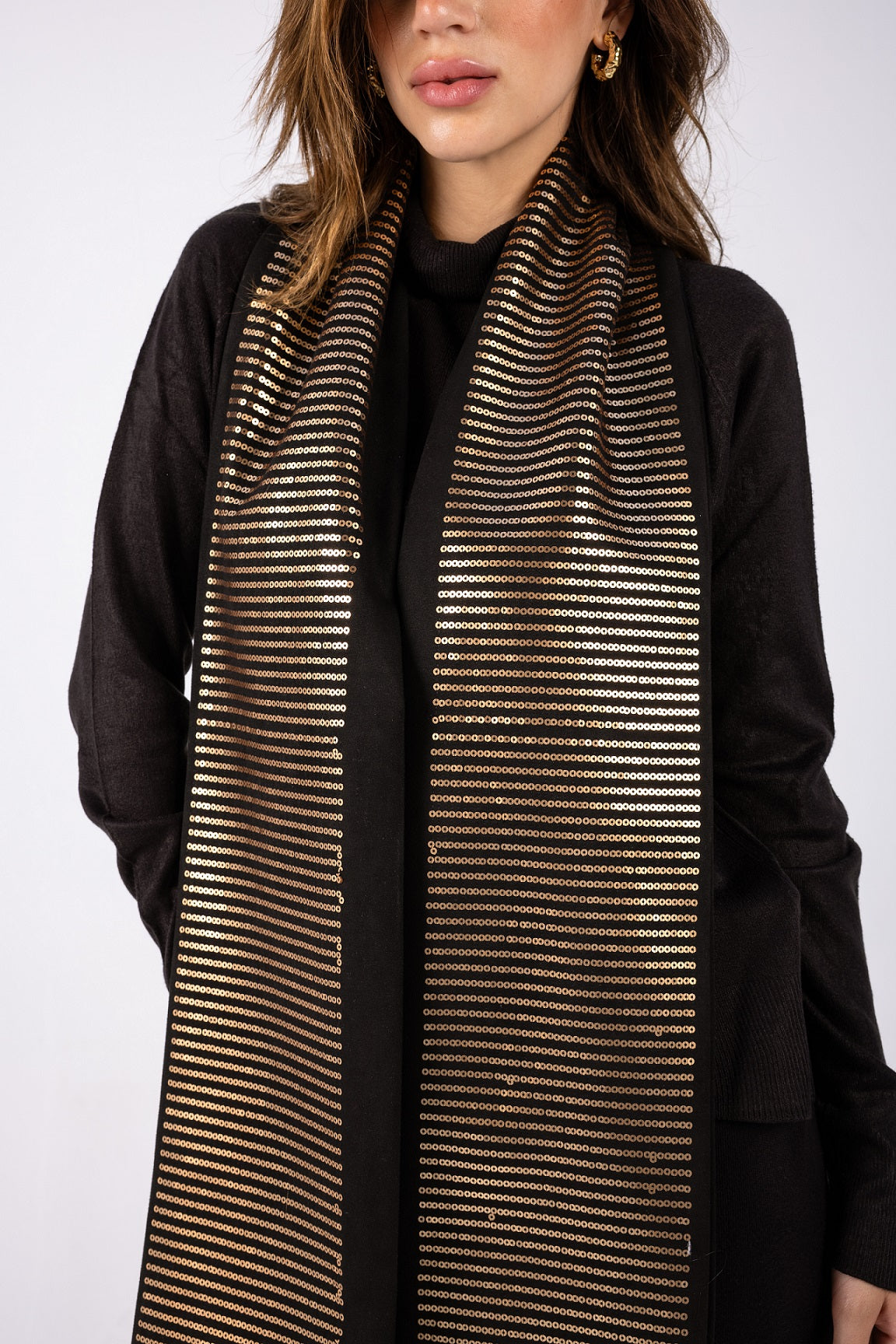 Woman wearing a black and gold striped scarf against a white background