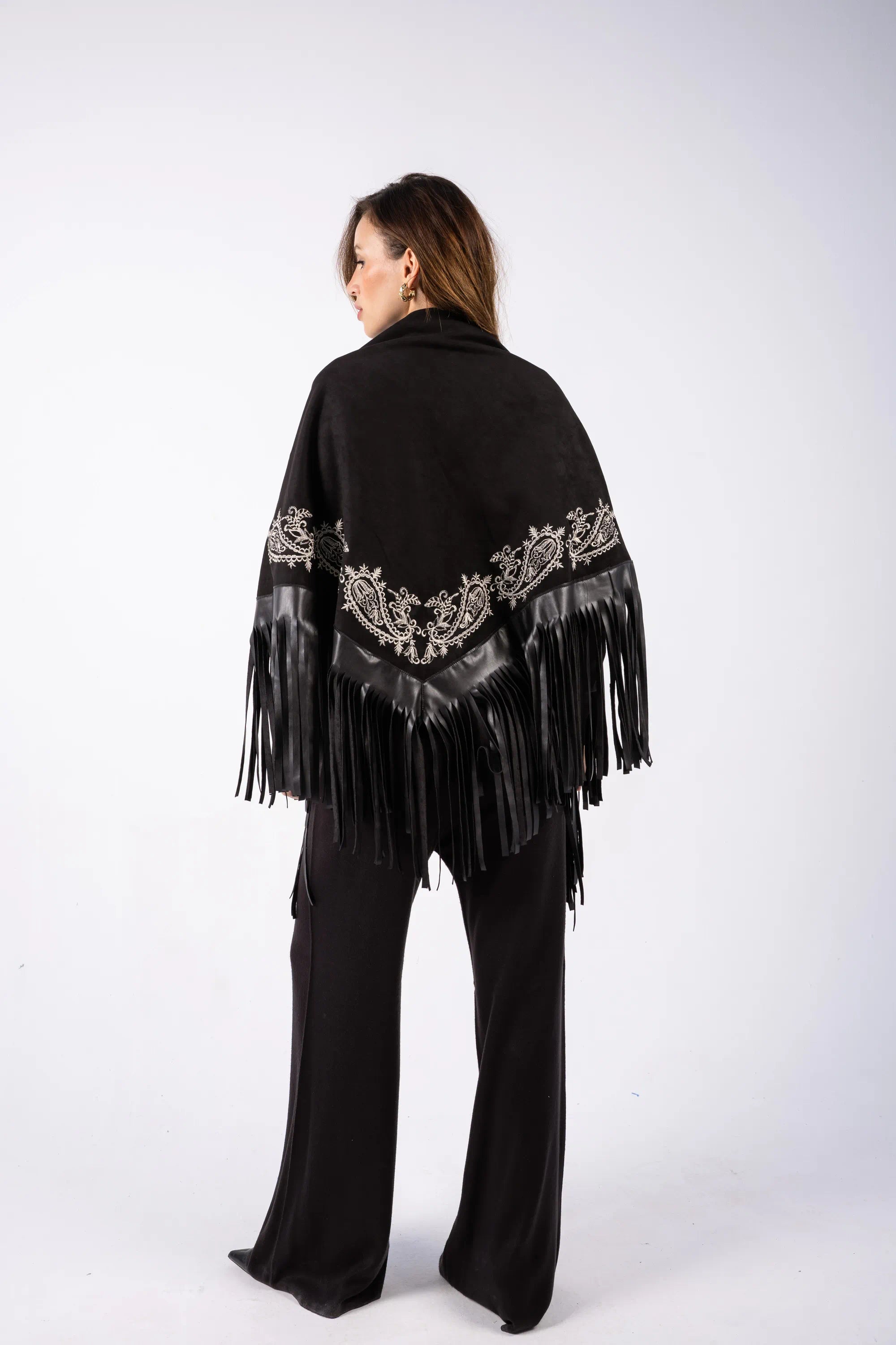 Woman wearing a black poncho with fringe and embroidery on a white background