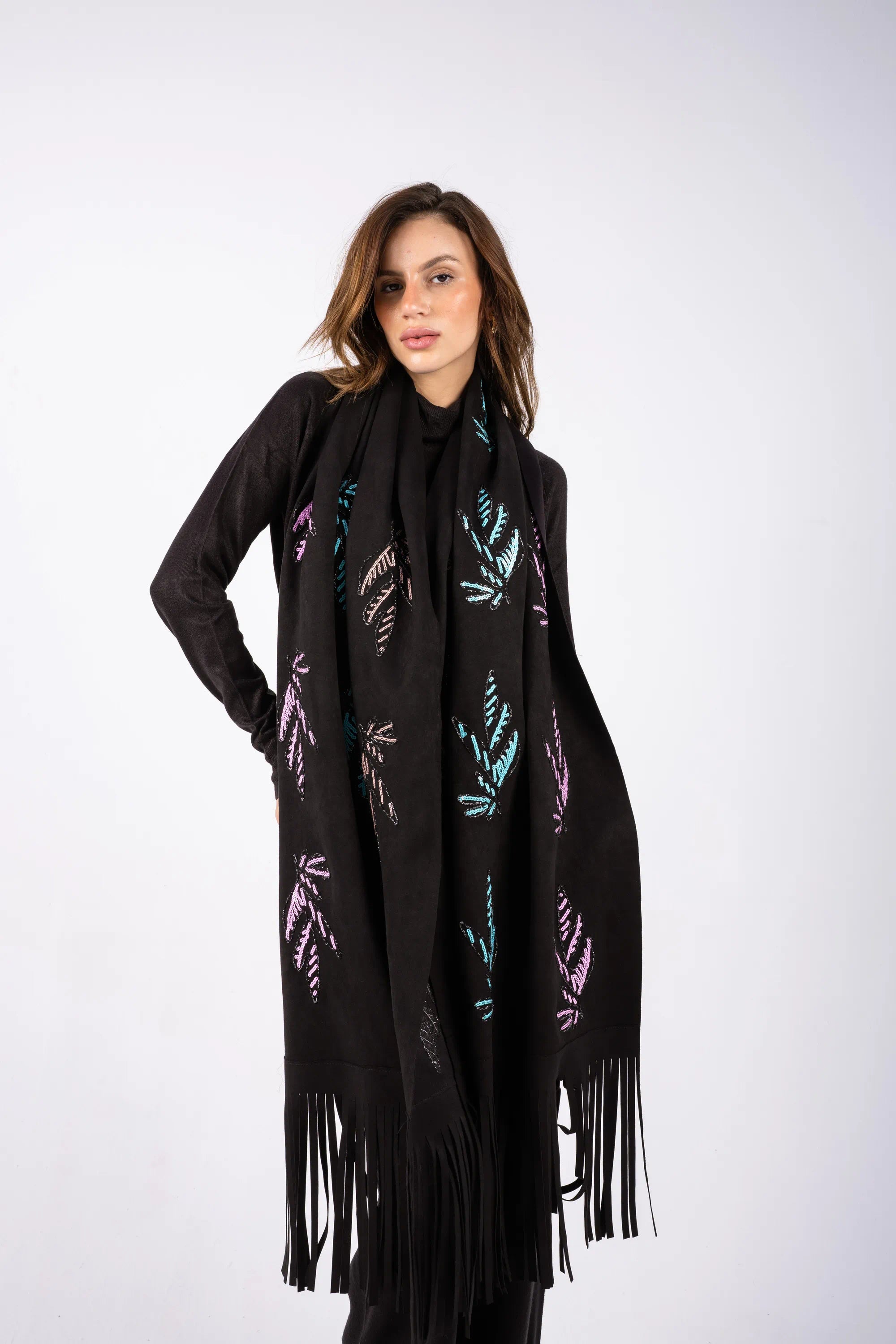 Woman wearing a black scarf with colorful leaf patterns and fringes on a white background