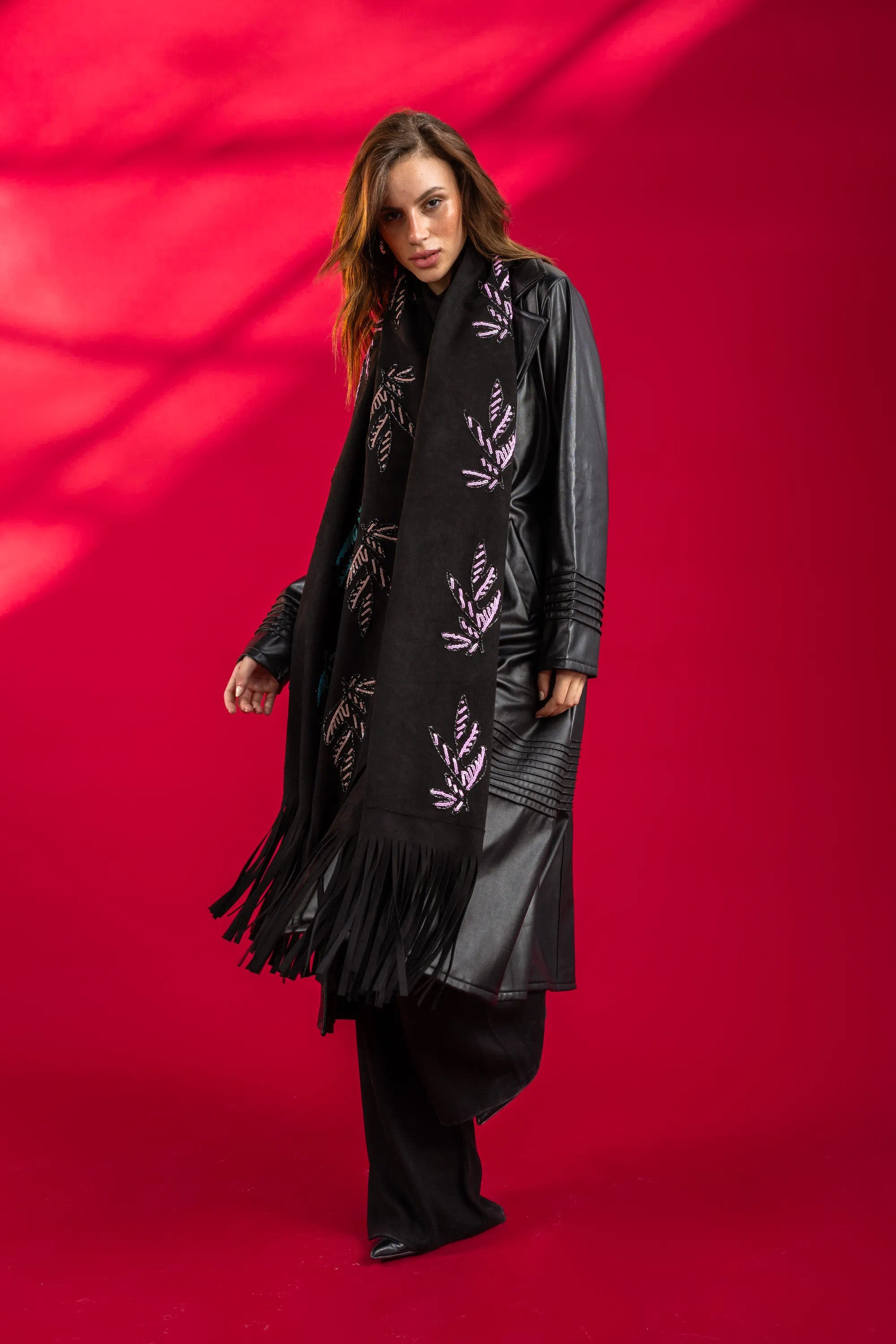 Woman wearing a black coat with a patterned scarf against a red background