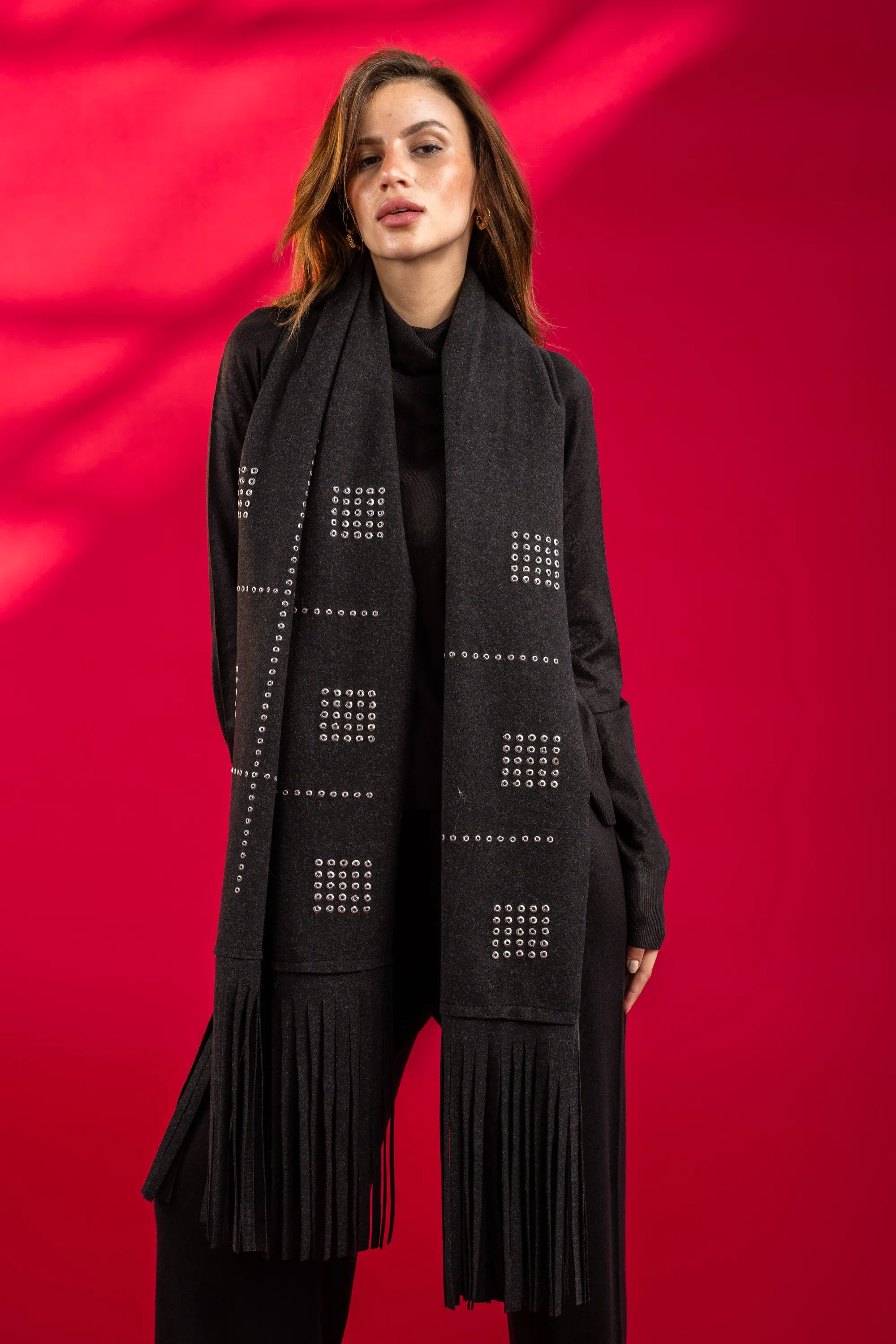 Woman wearing a black scarf with geometric patterns and fringes against a red background
