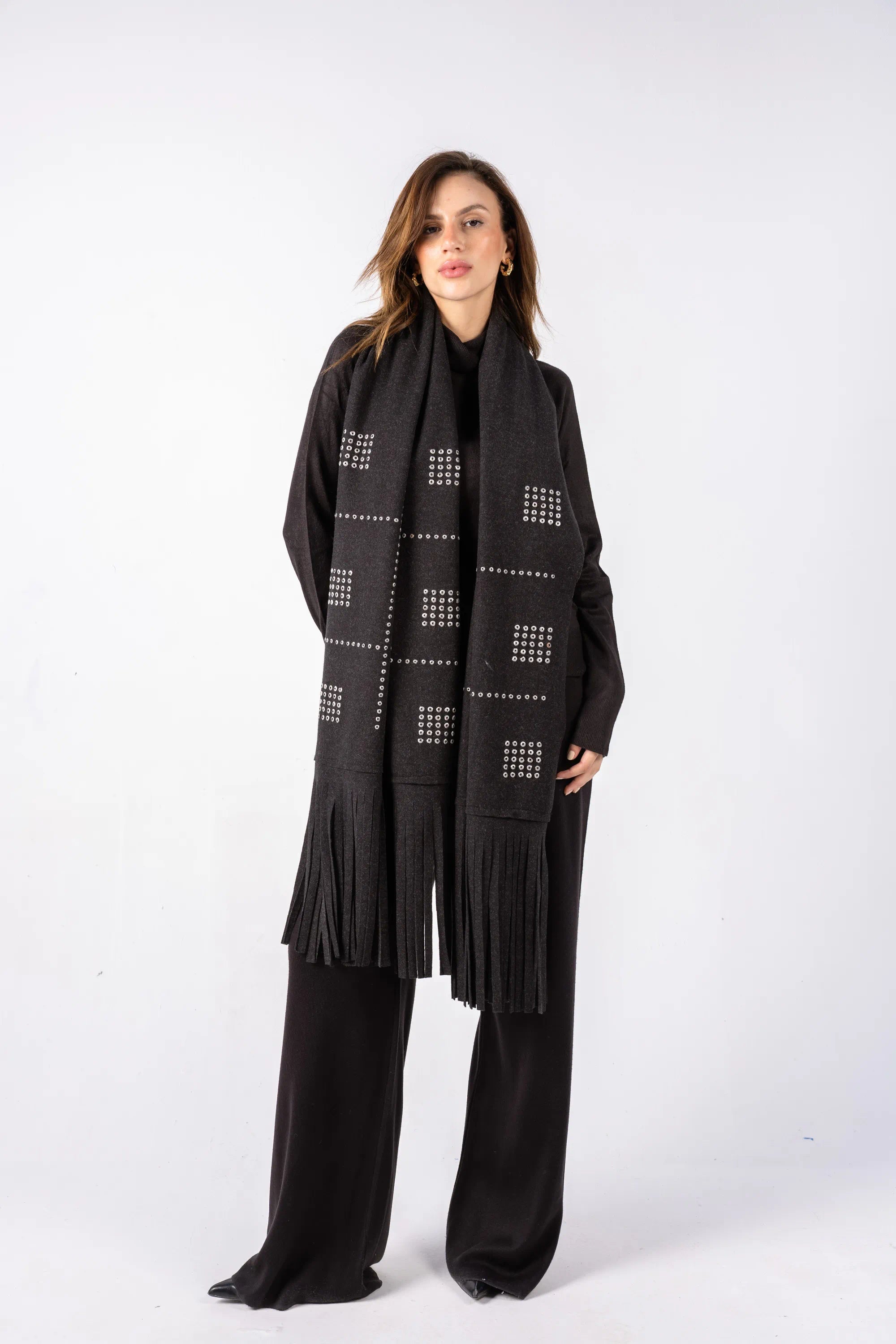 Woman wearing a long black scarf with geometric patterns and fringes on a white background